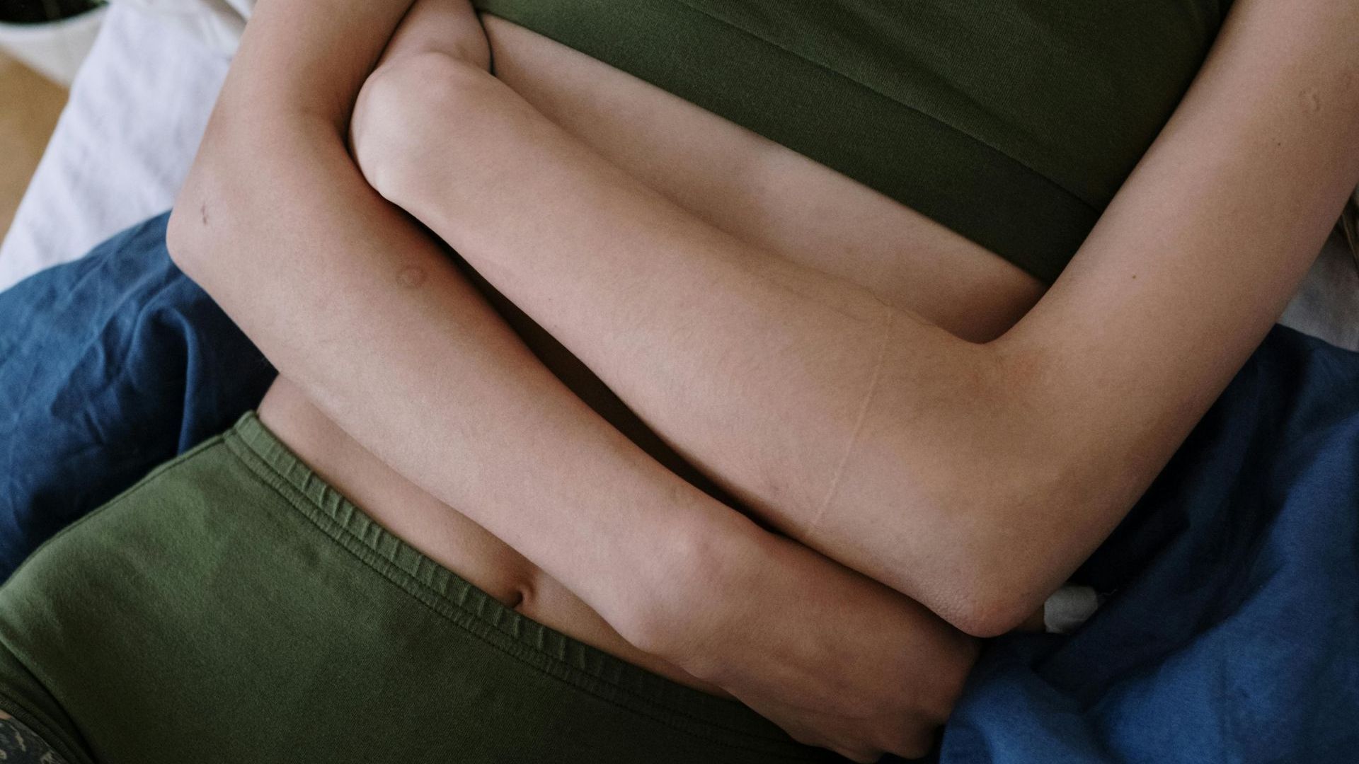 A woman is laying on a bed with her hands on her stomach.