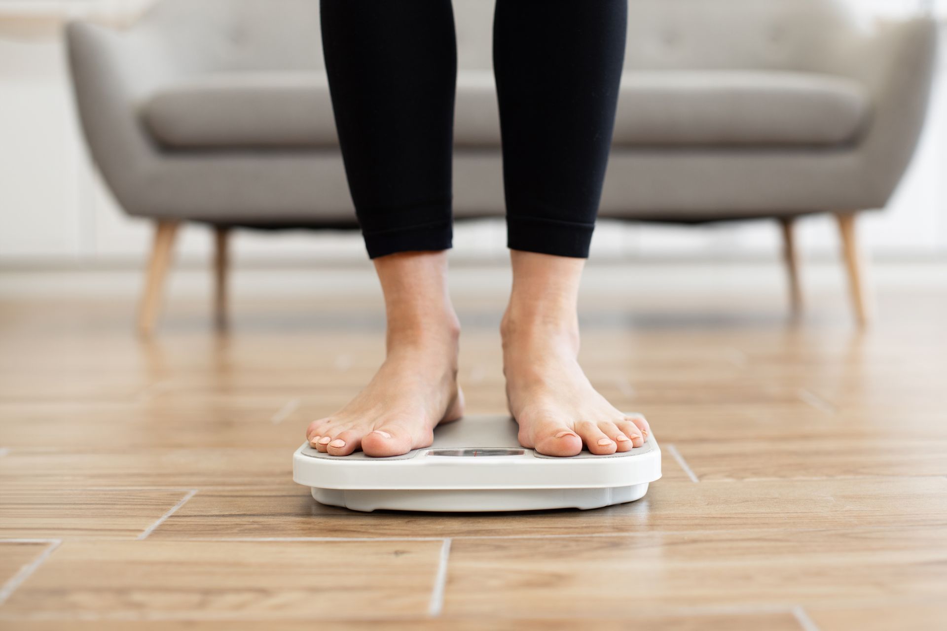 A woman is standing on a scale in front of a couch.