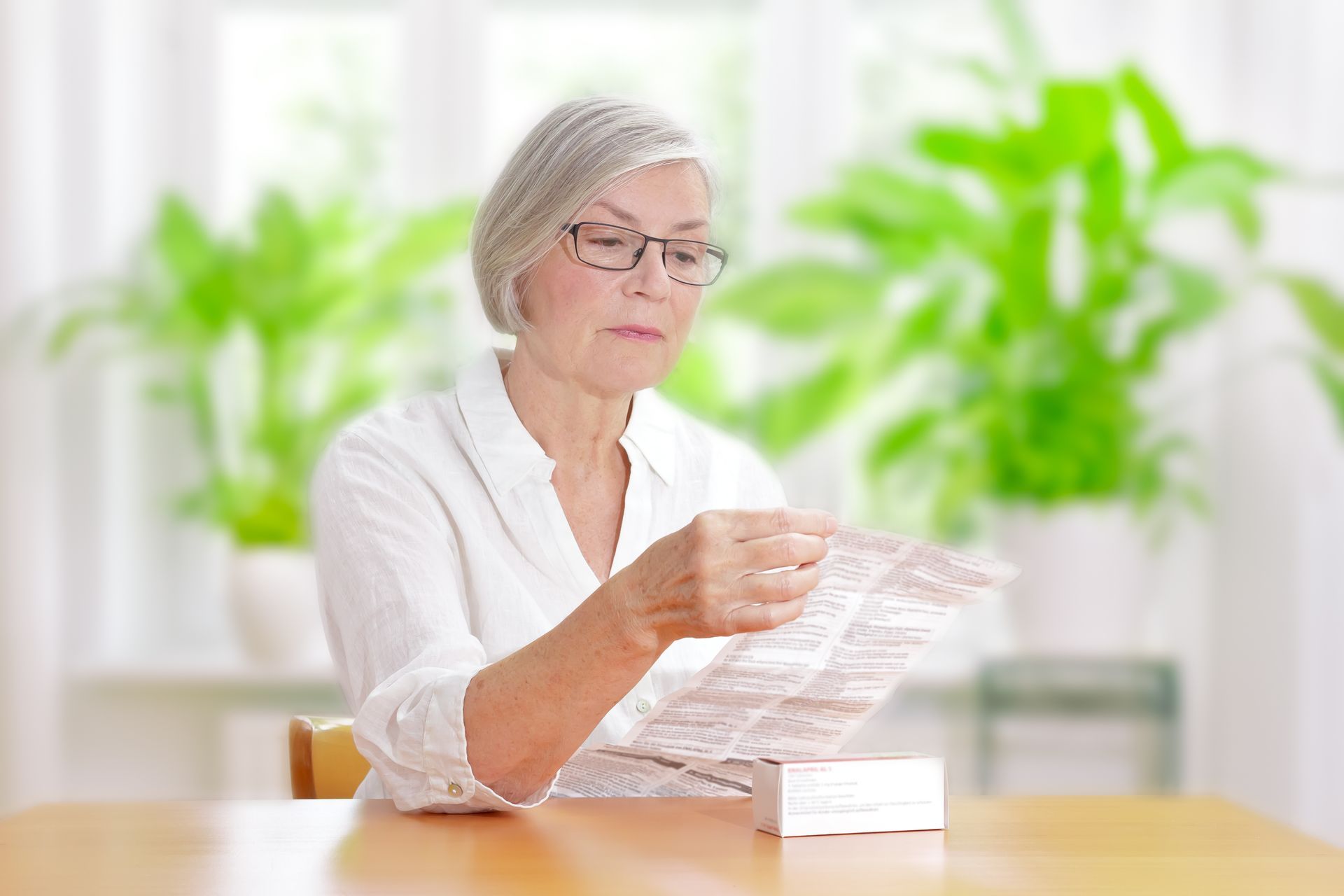 An elderly woman is sitting at a table reading a newspaper.