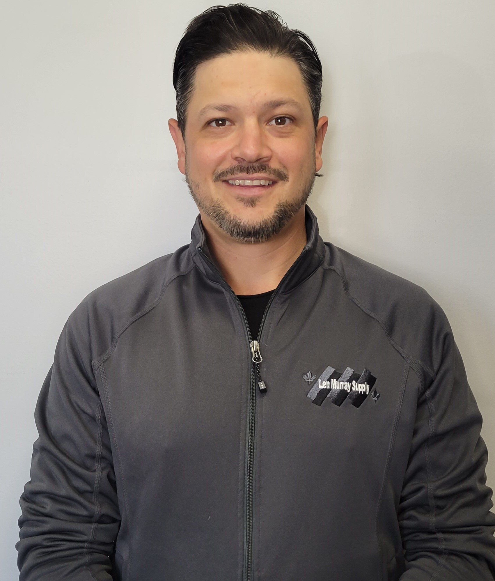 A man with a beard is wearing a grey jacket and smiling for the camera.