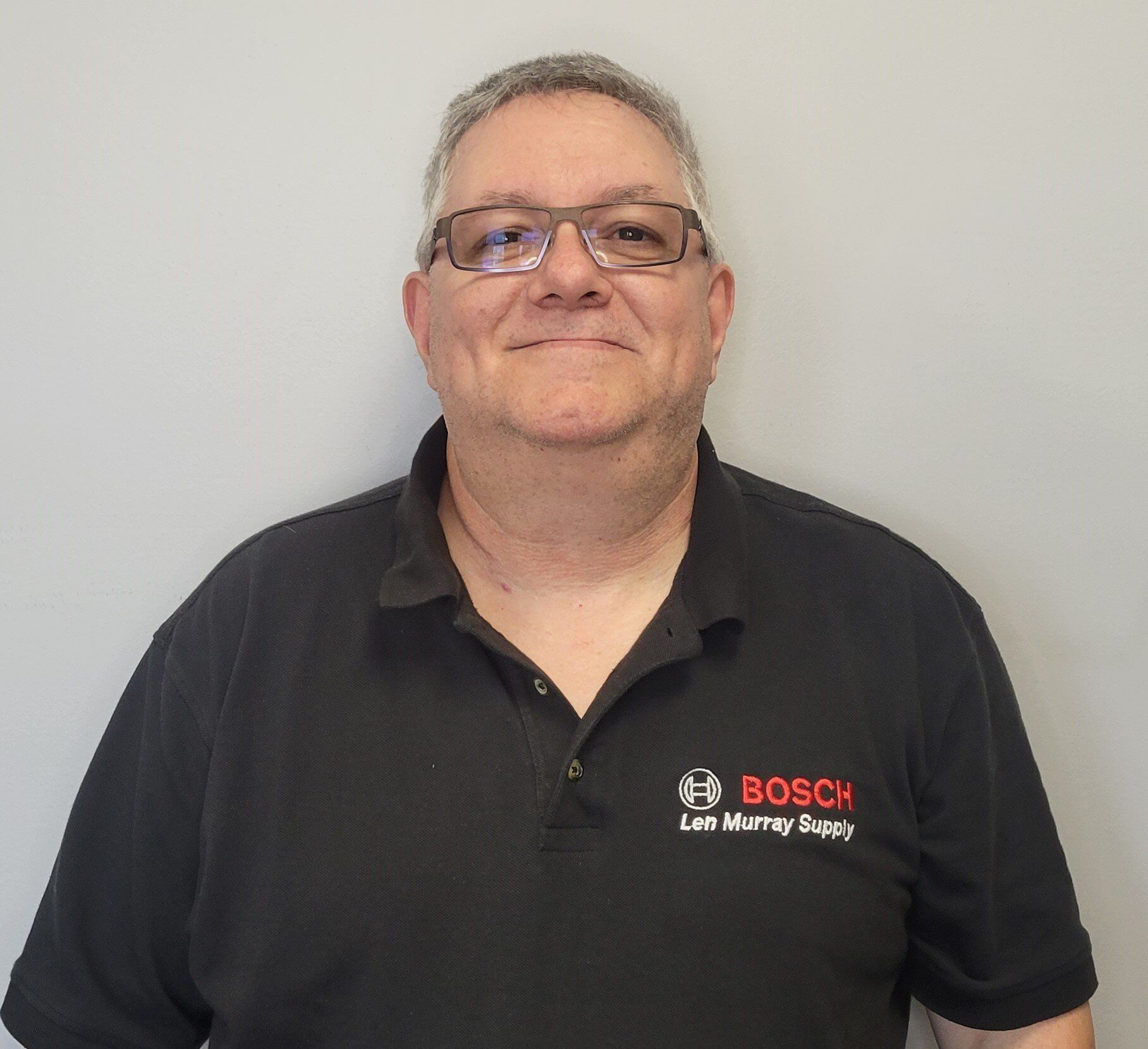 A man wearing glasses and a bosch shirt is smiling for the camera.