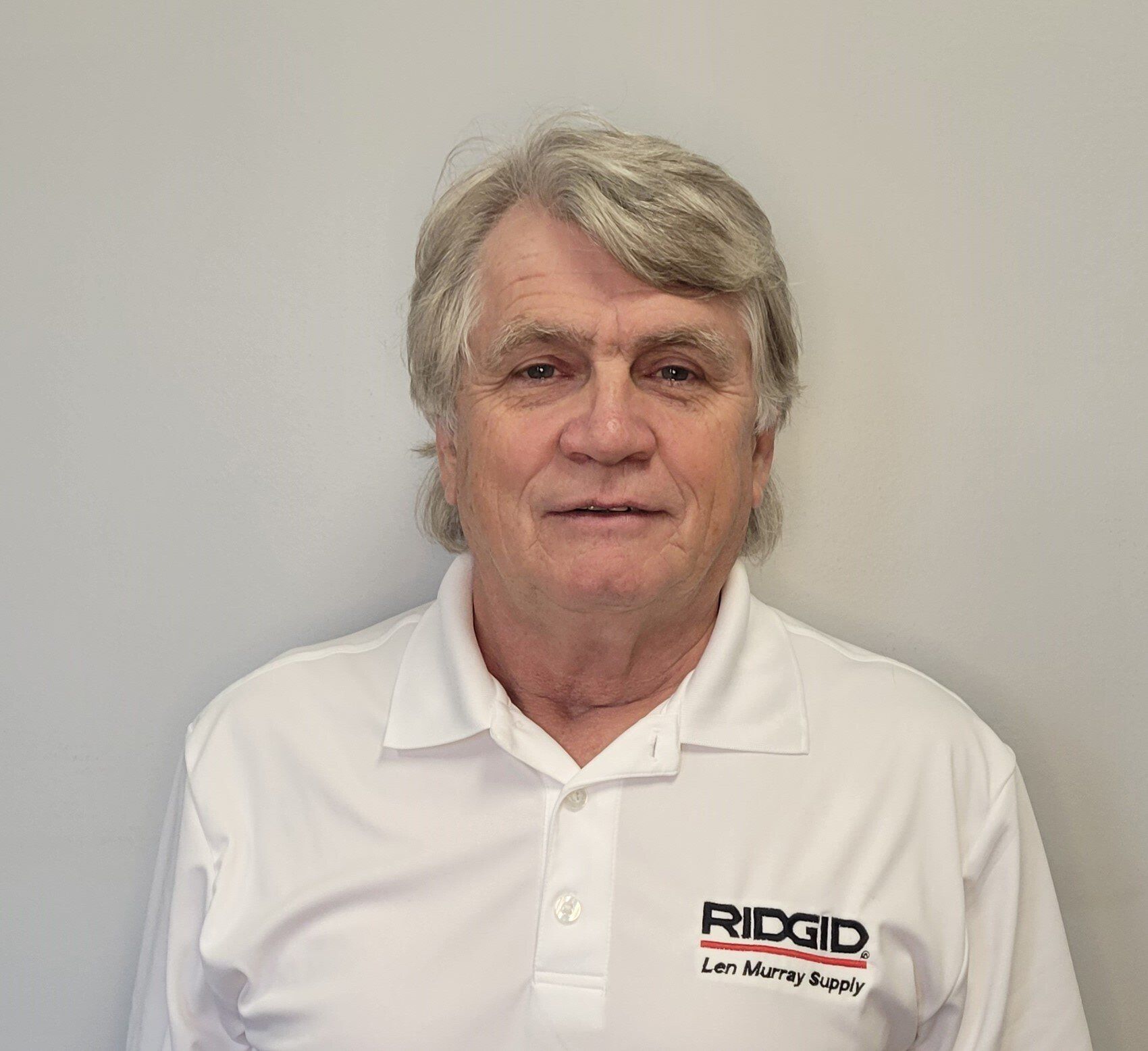 A man wearing a white polo shirt is standing in front of a white wall.
