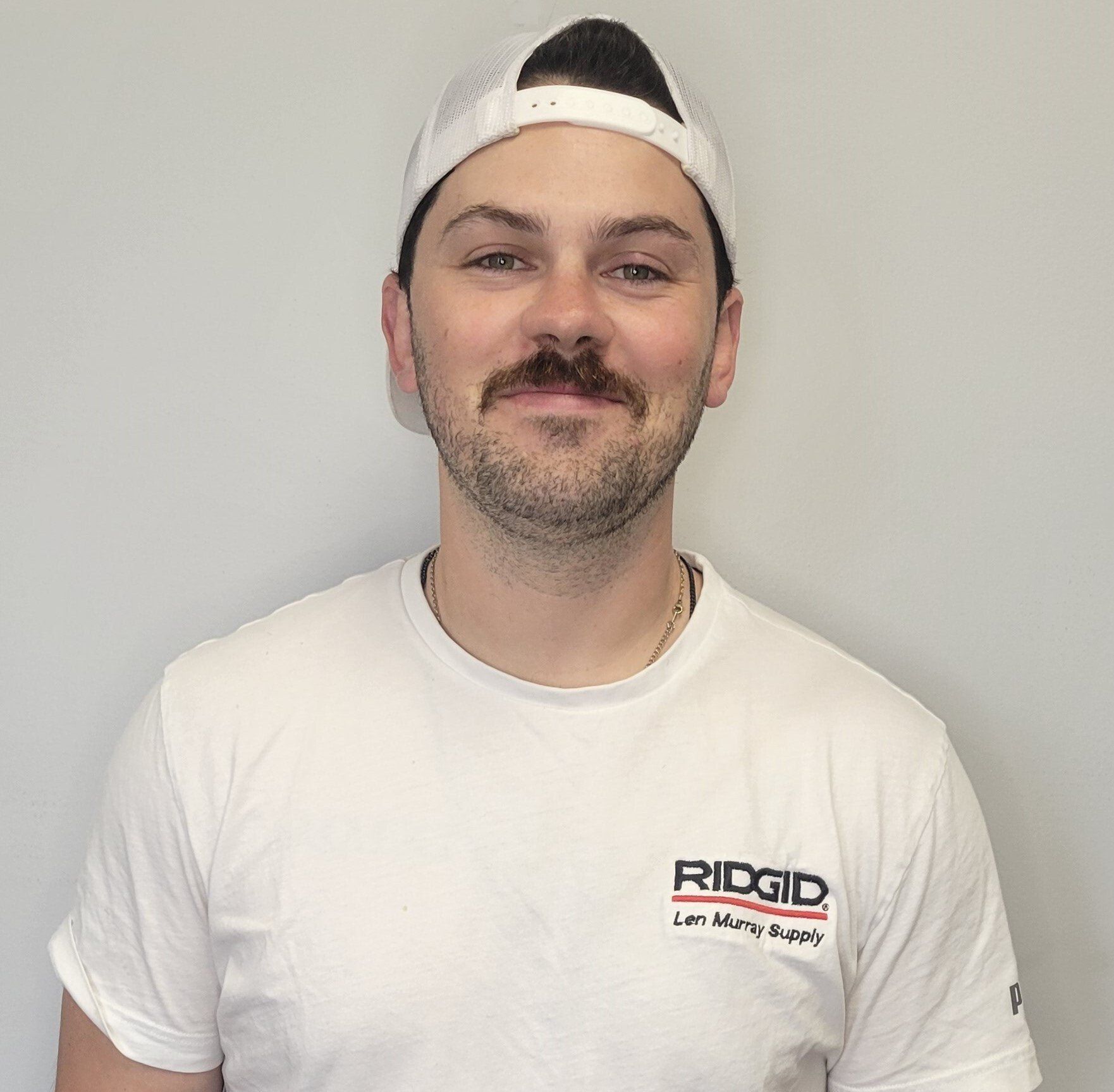 A man wearing a white hat and a white t-shirt with the word ridgid on it.