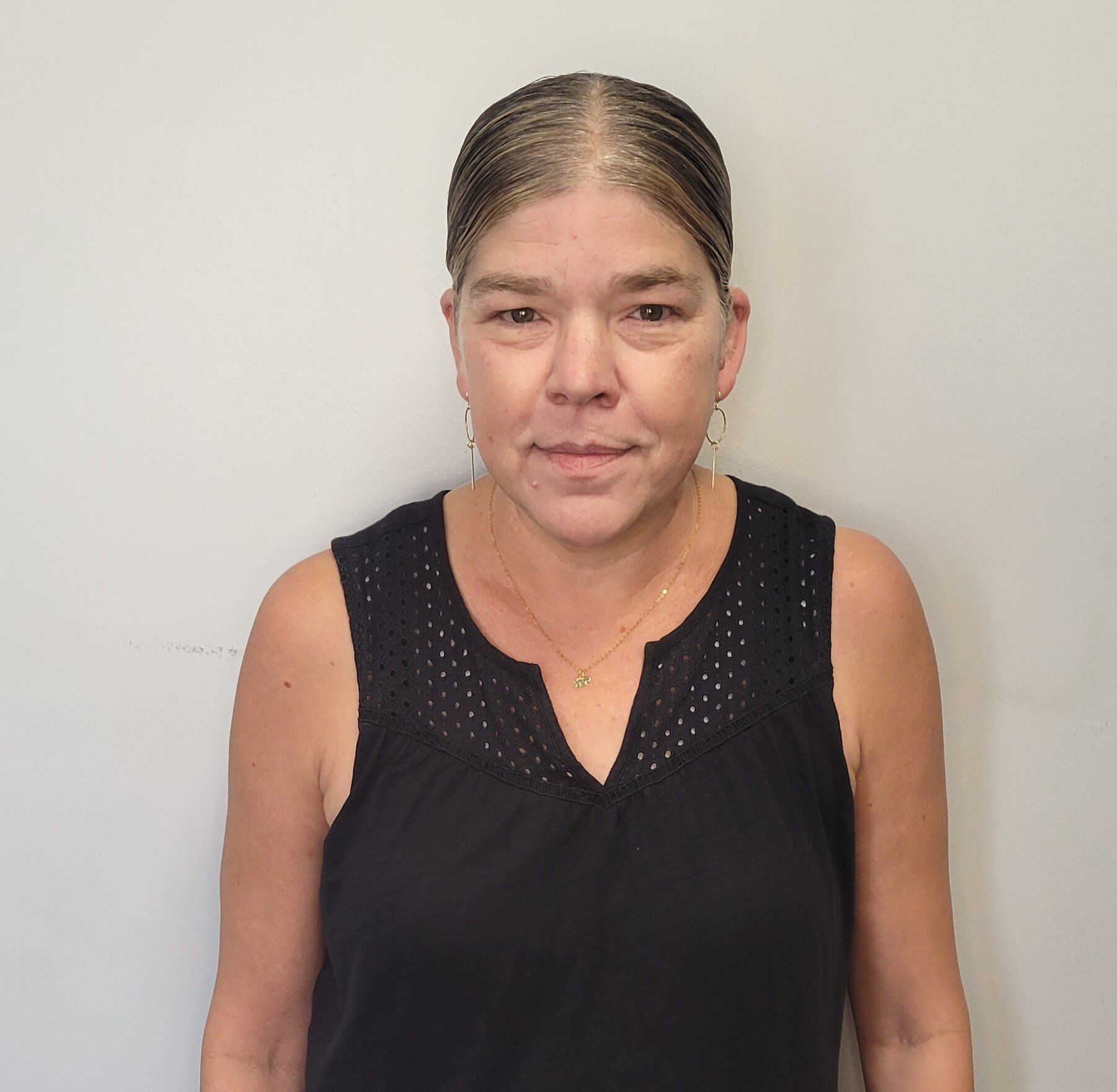 A woman in a black tank top is standing in front of a white wall.
