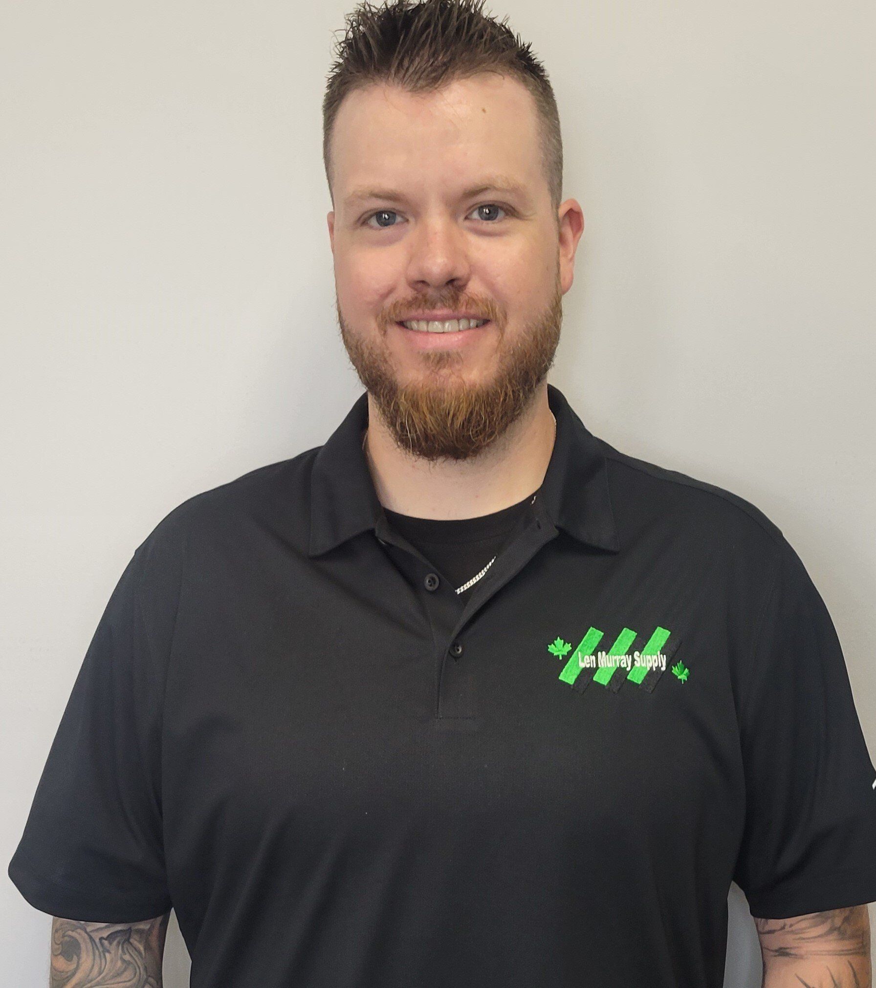 A man with a beard is wearing a black shirt with a green logo on it.