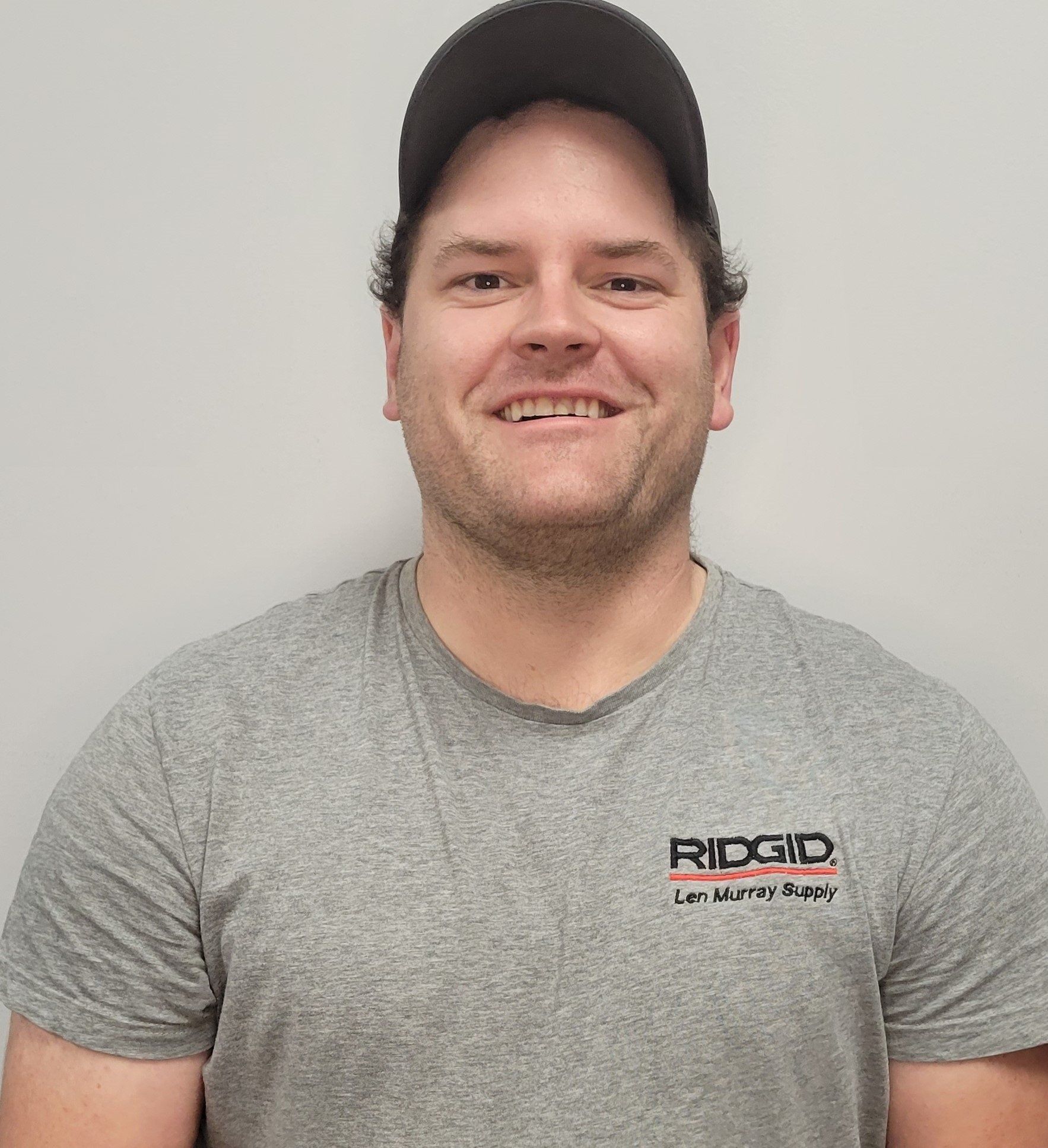 A man wearing a gray t-shirt and a black hat is smiling for the camera.