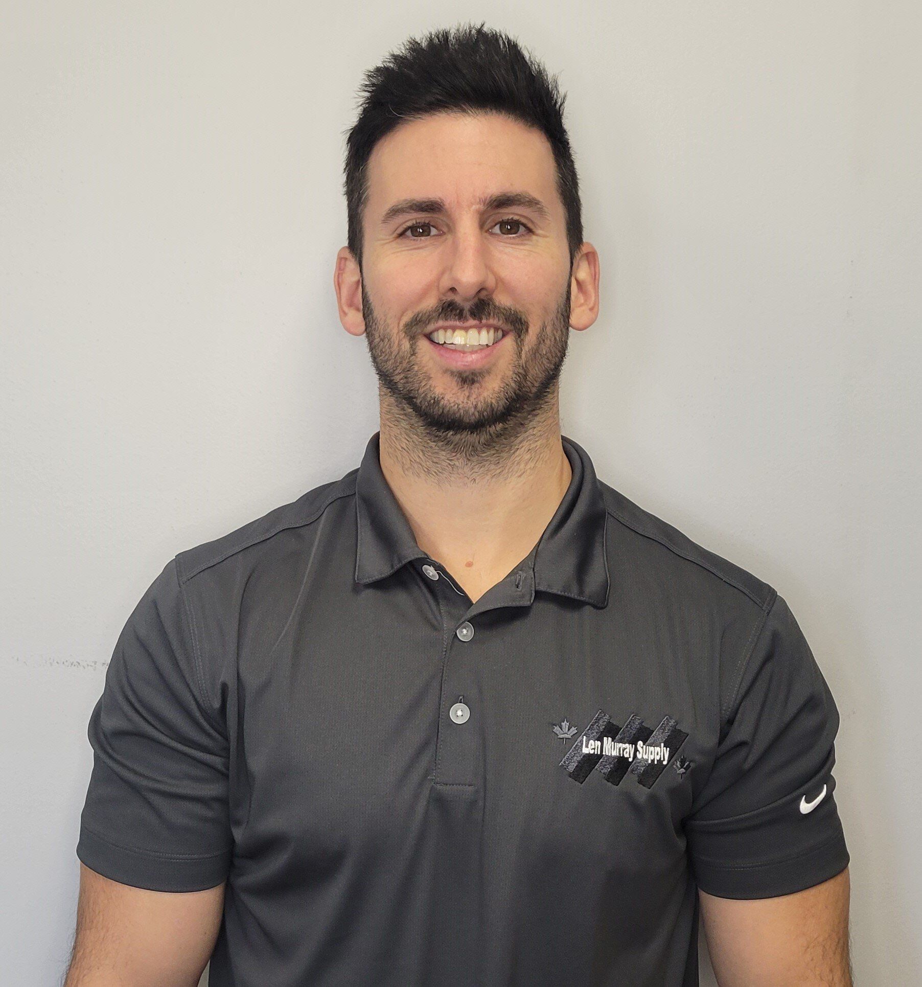 A man with a beard is wearing a black polo shirt and smiling.