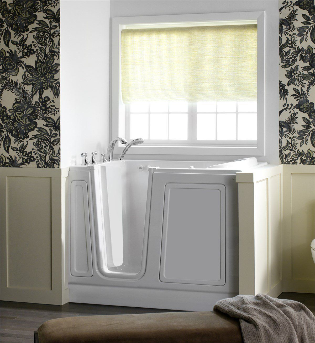 A white walk-in bathtub with a window above it, set against floral wallpaper and cream-colored panels.