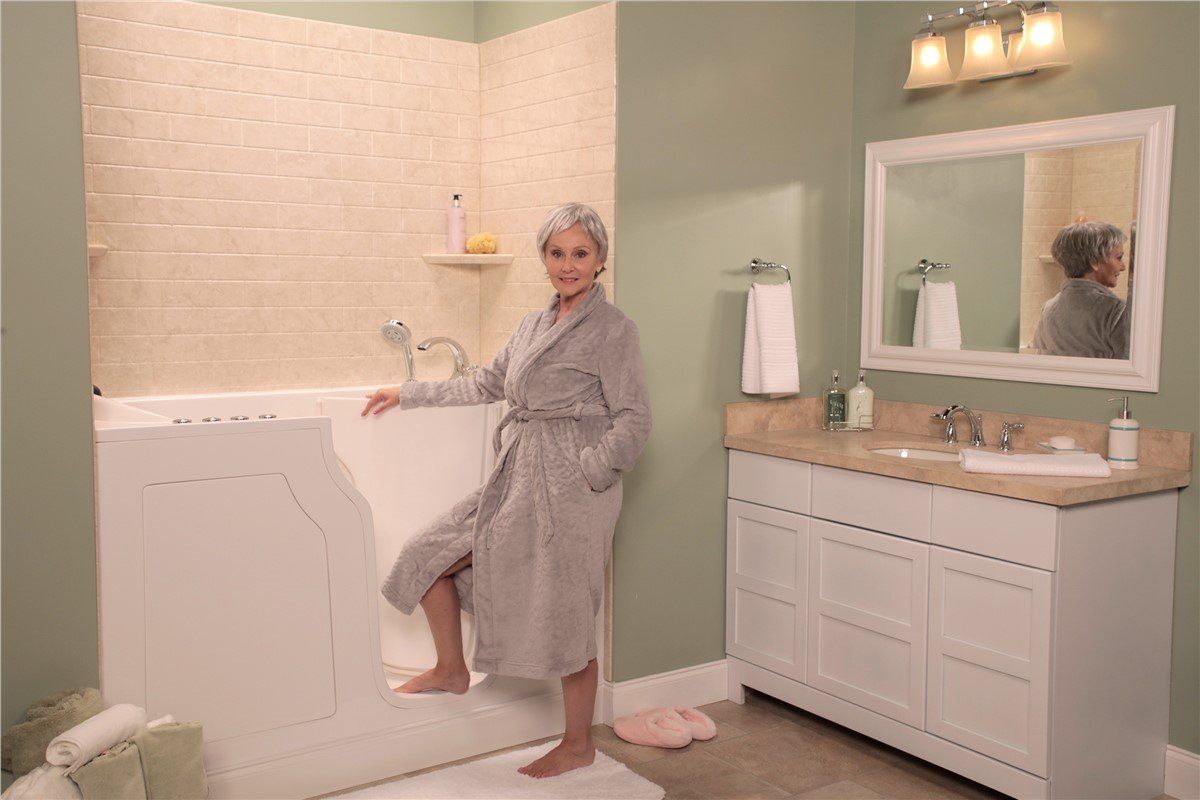 Woman in a robe stepping into a walk-in bathtub in a bathroom. The tub is white, and the walls are light green.