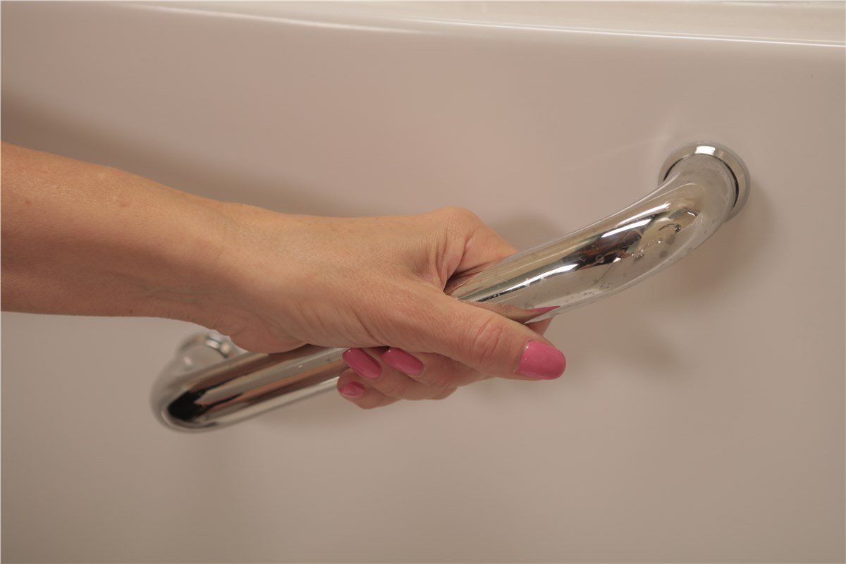 A person's hand gripping a silver grab bar installed on a white surface, likely in a bathroom.