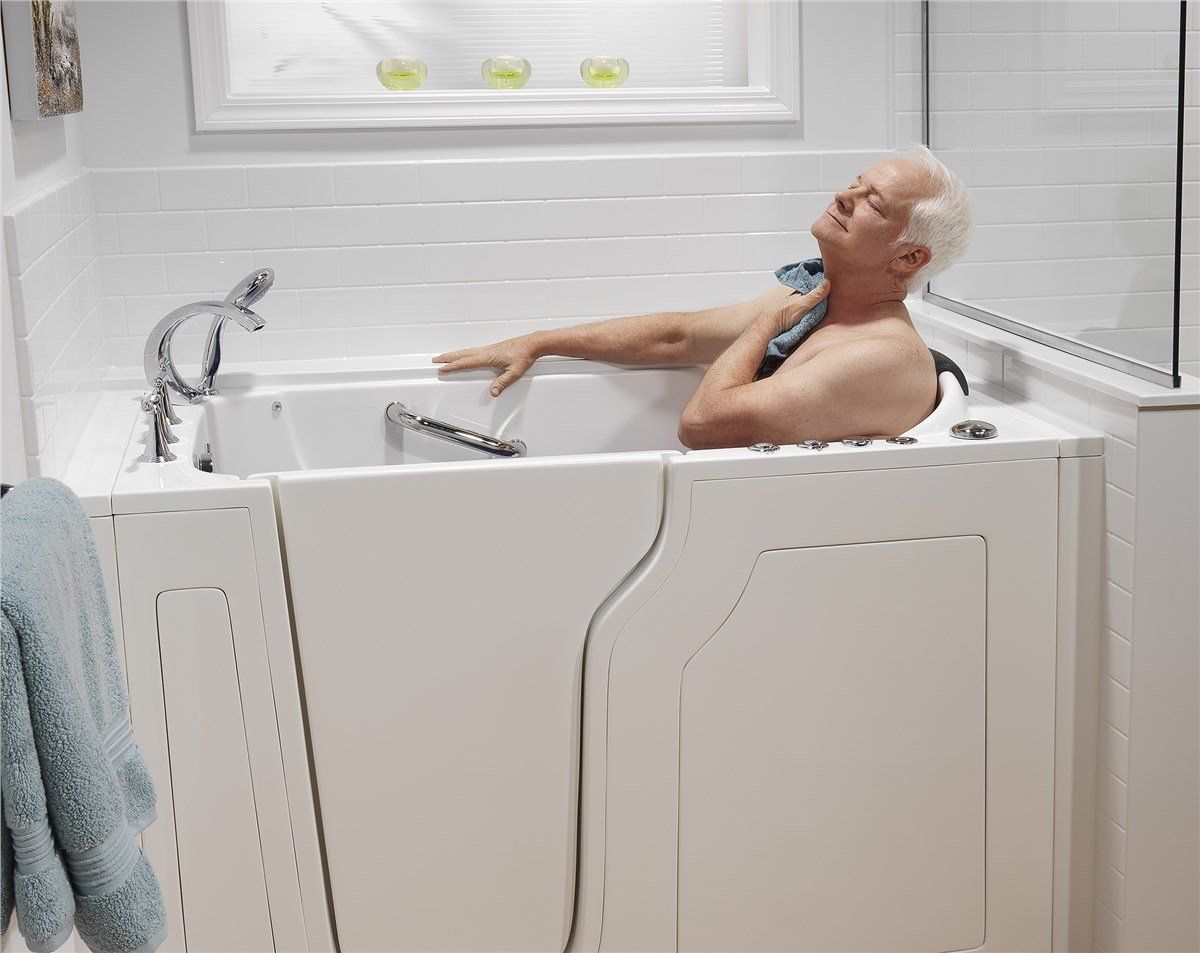 Elderly man relaxes in a white walk-in tub, eyes closed, holding a towel in a peaceful bathroom setting.