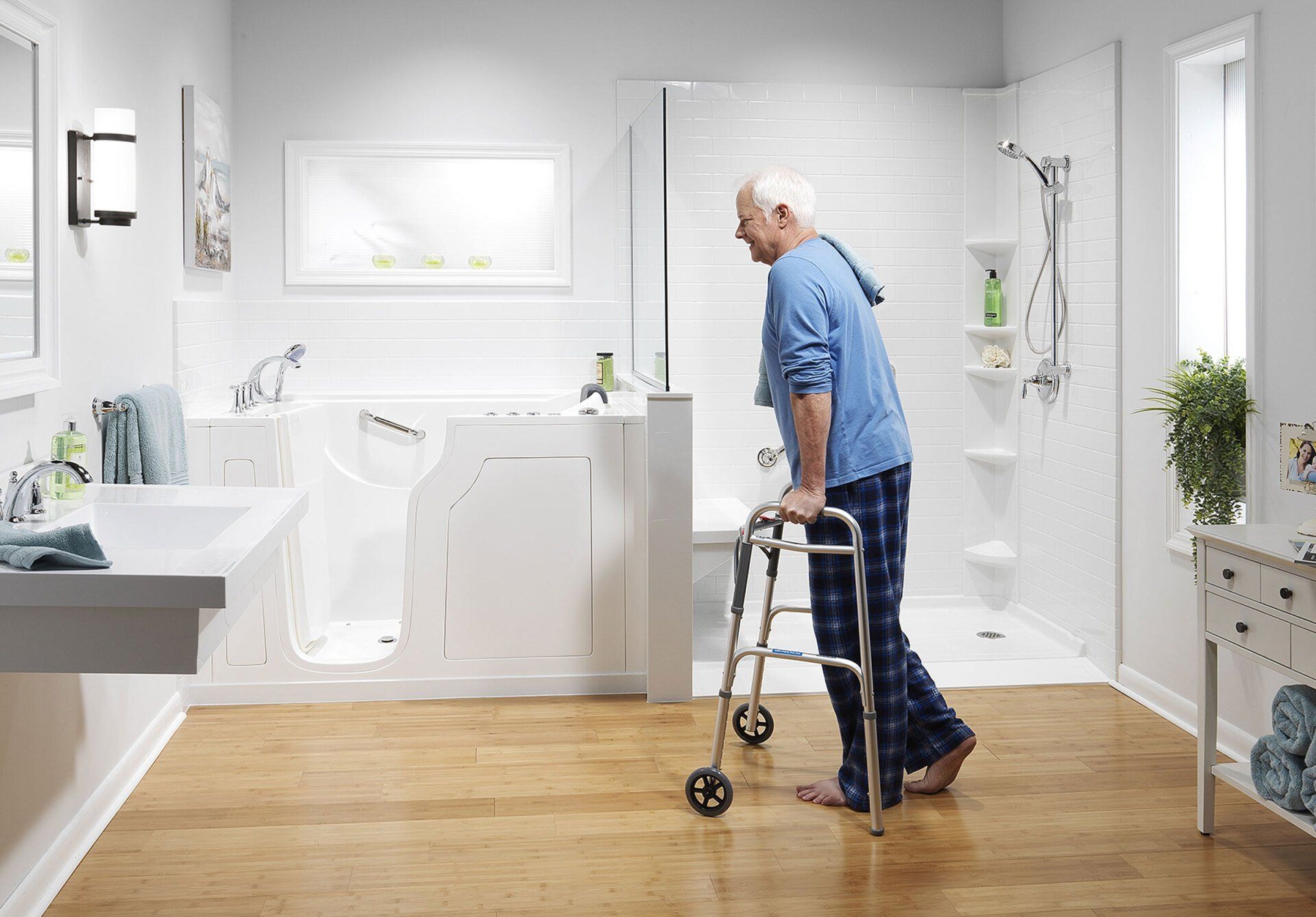 An elderly man using a walker enters a brightly lit, accessible bathroom with a walk-in tub and safety bars.