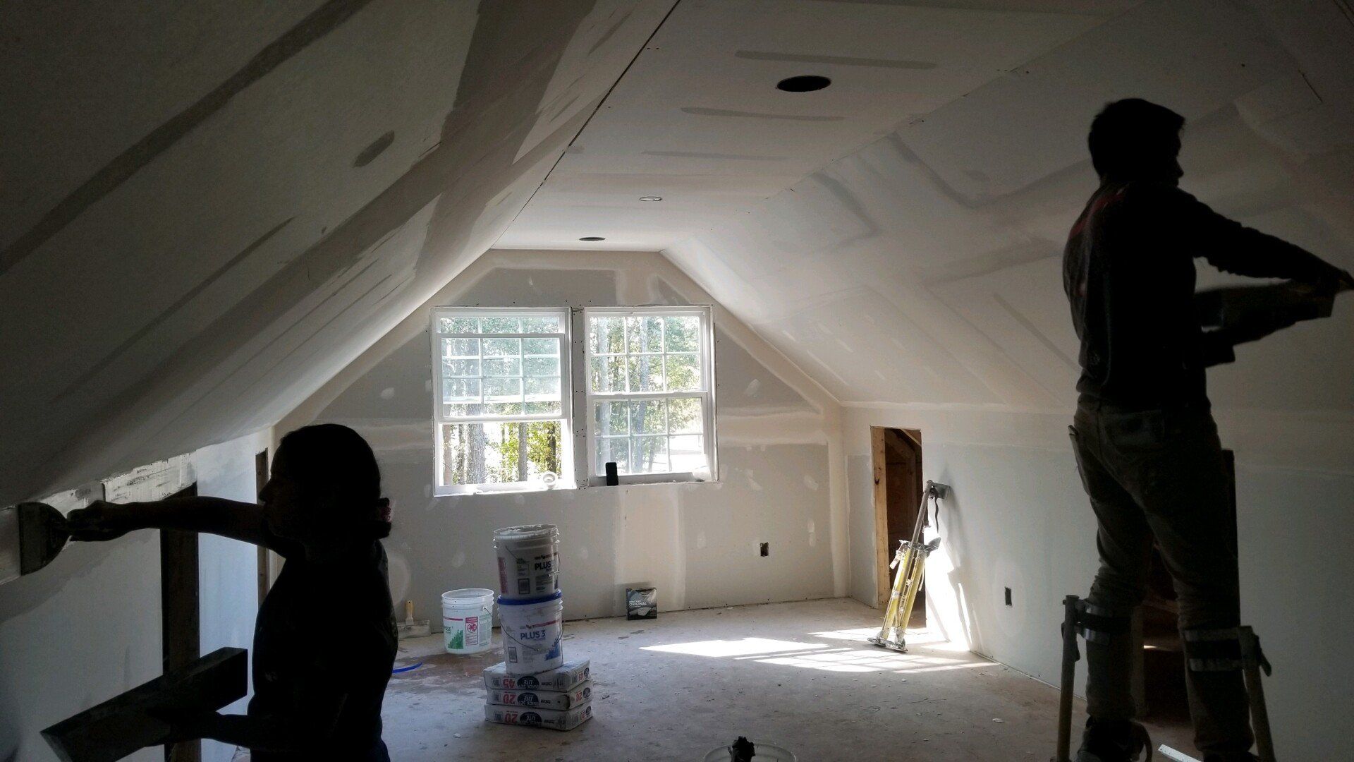 two men are working in a room that has a stack of buckets of paint on the floor