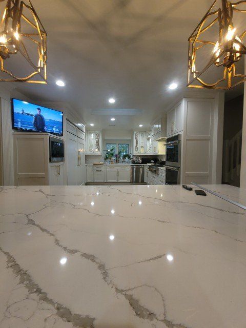 a kitchen with white cabinets , stainless steel appliances , a marble counter top and a flat screen tv .