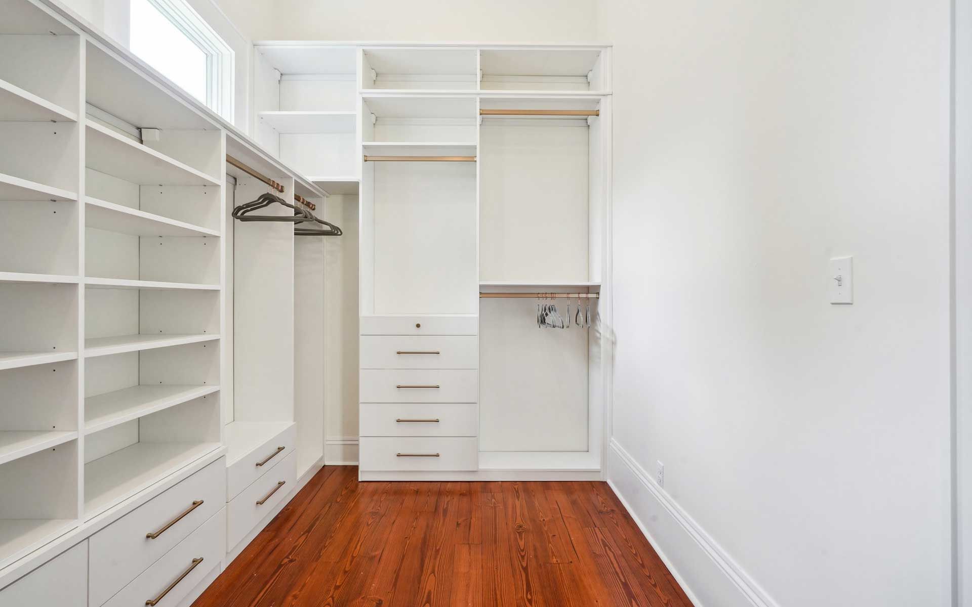 A walk in closet with wooden floors and white shelves.