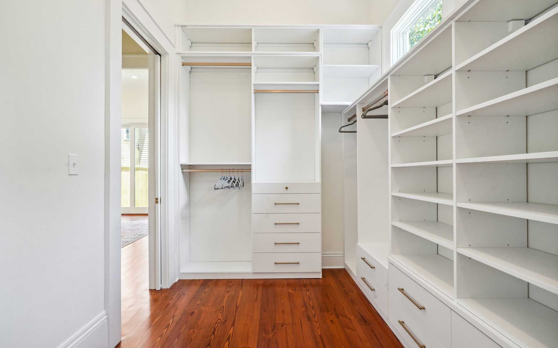 A walk in closet with wooden floors and white shelves.