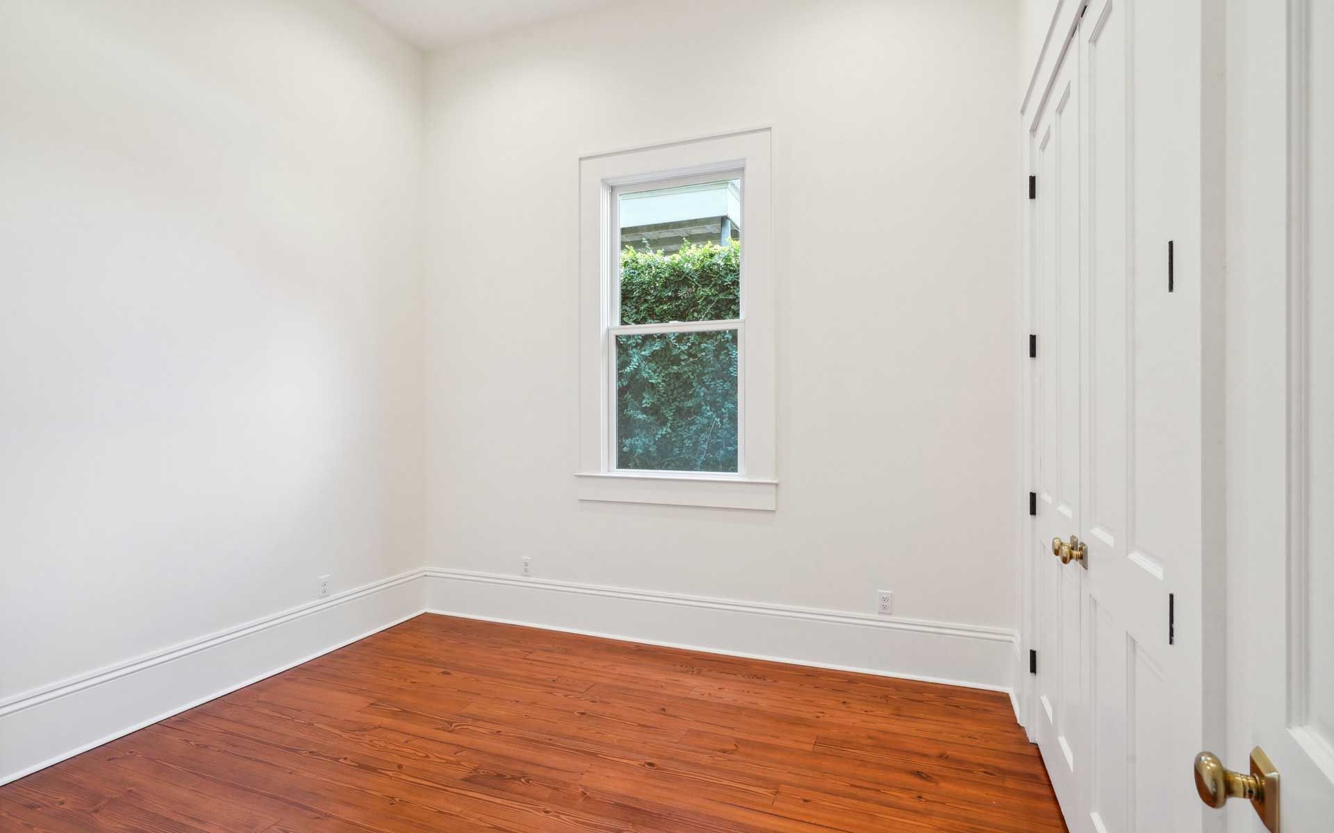 An empty room with hardwood floors , white walls and a window.