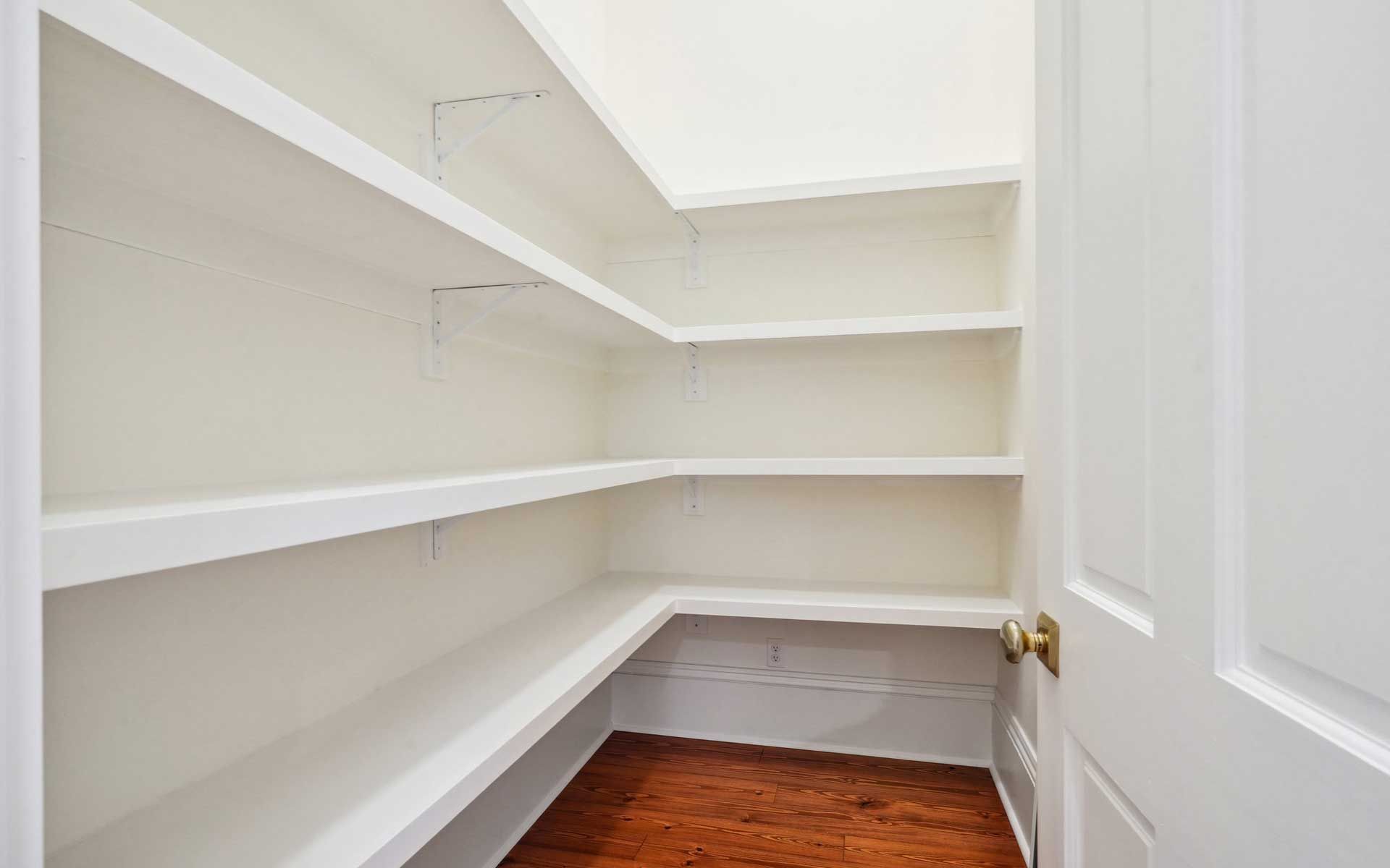 An empty pantry with wooden floors and white shelves