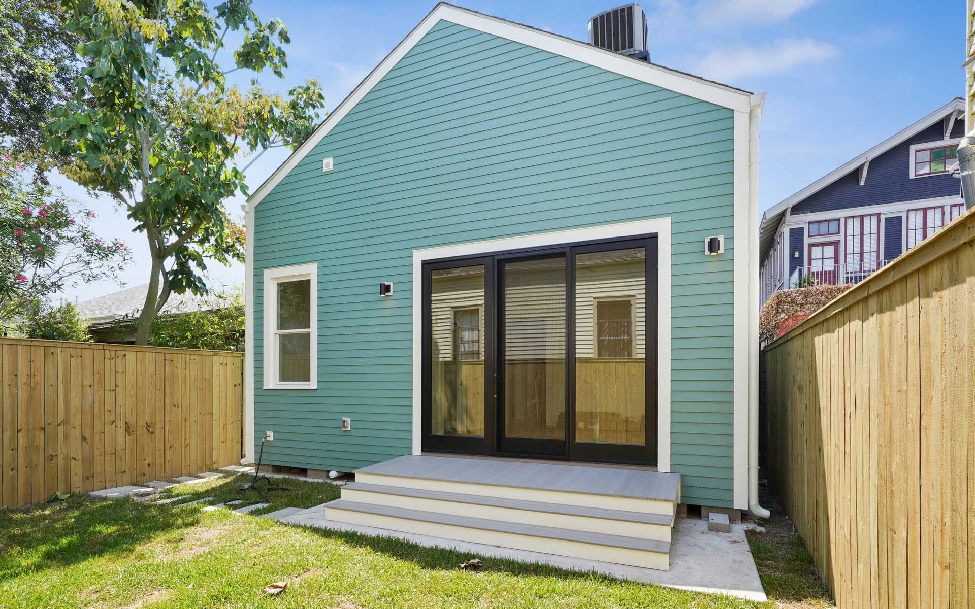 The back of a green house with sliding glass doors and a wooden fence.