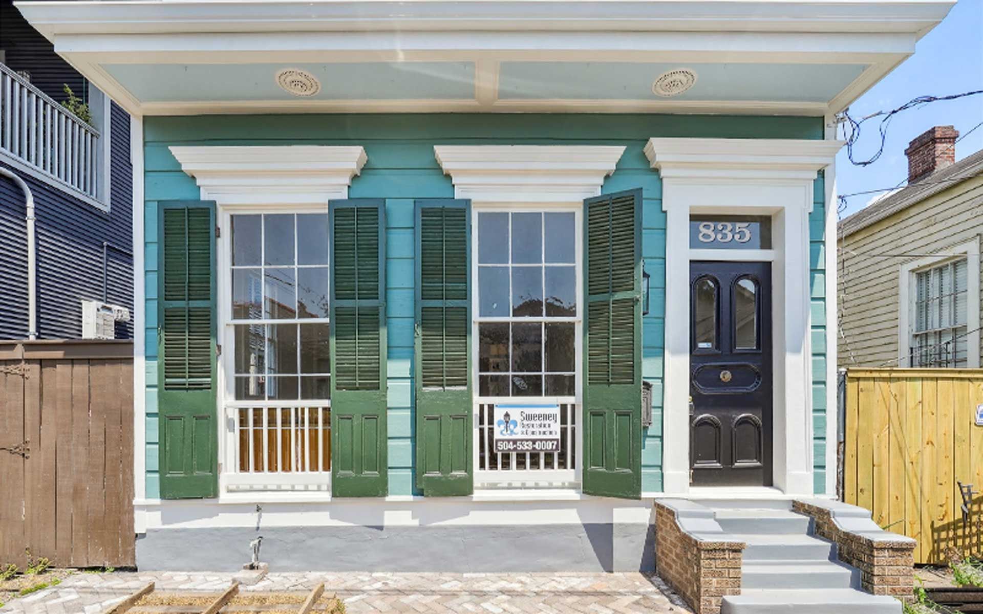 A blue house with green shutters and a black door