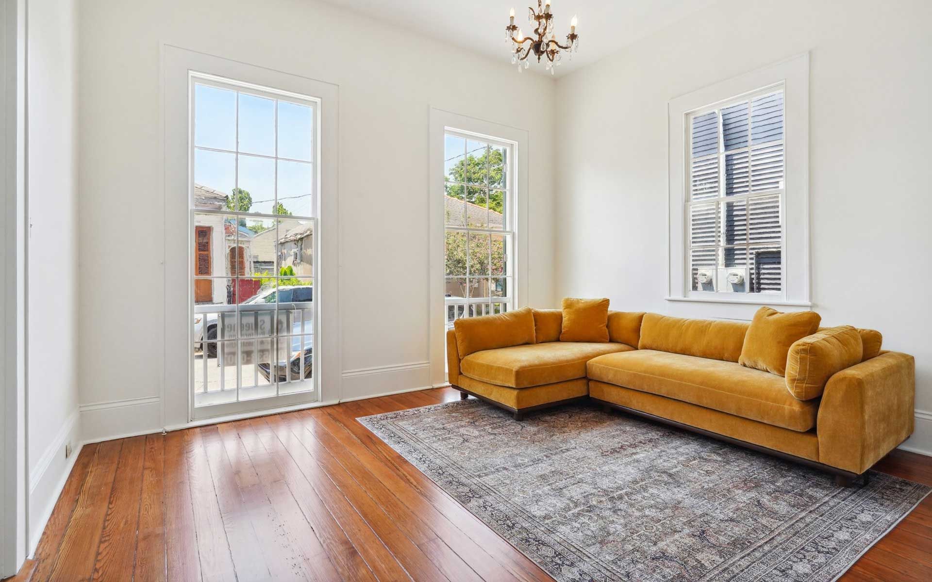 An empty living room with a yellow sectional couch and a rug.
