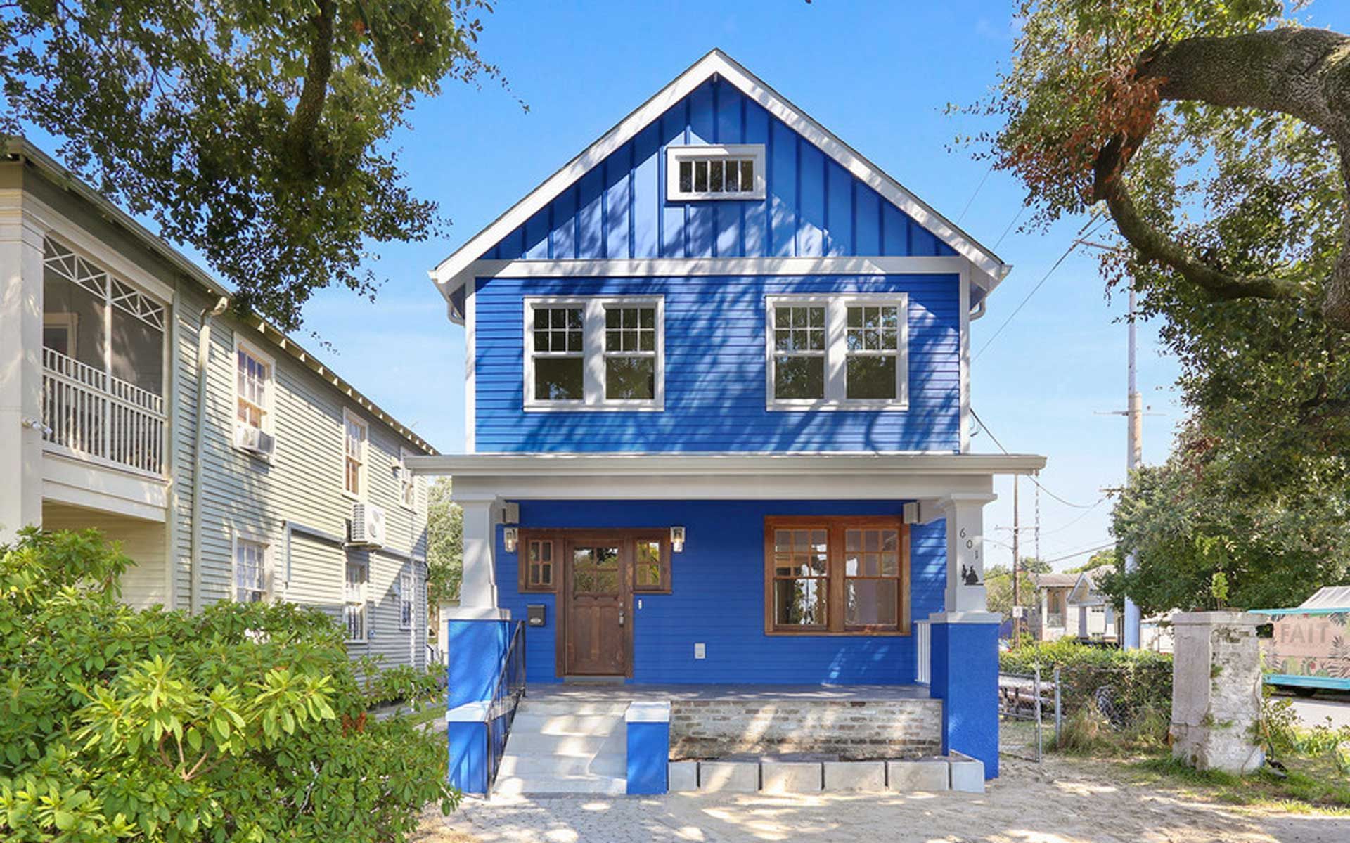 A blue house with a white trim is surrounded by trees and bushes.