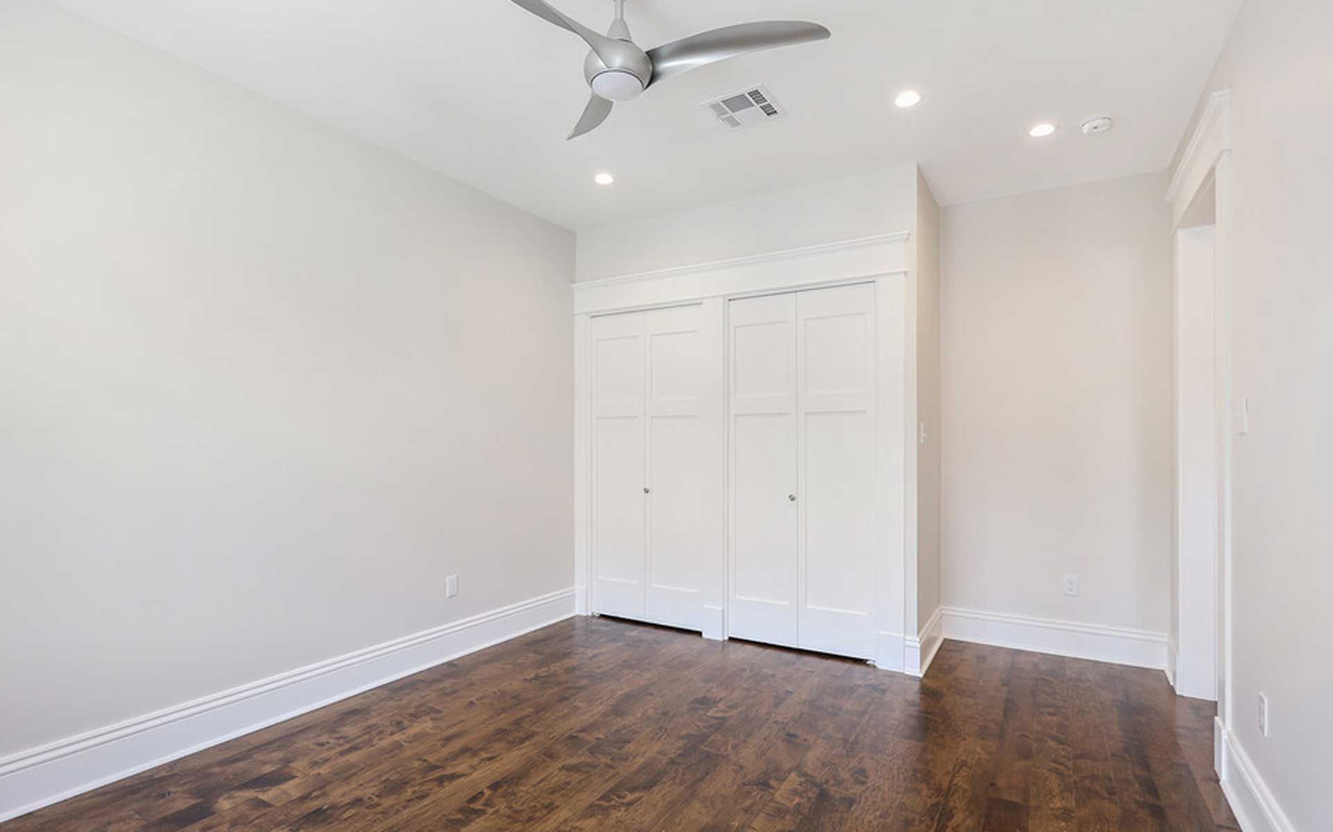 An empty bedroom with hardwood floors and a ceiling fan.