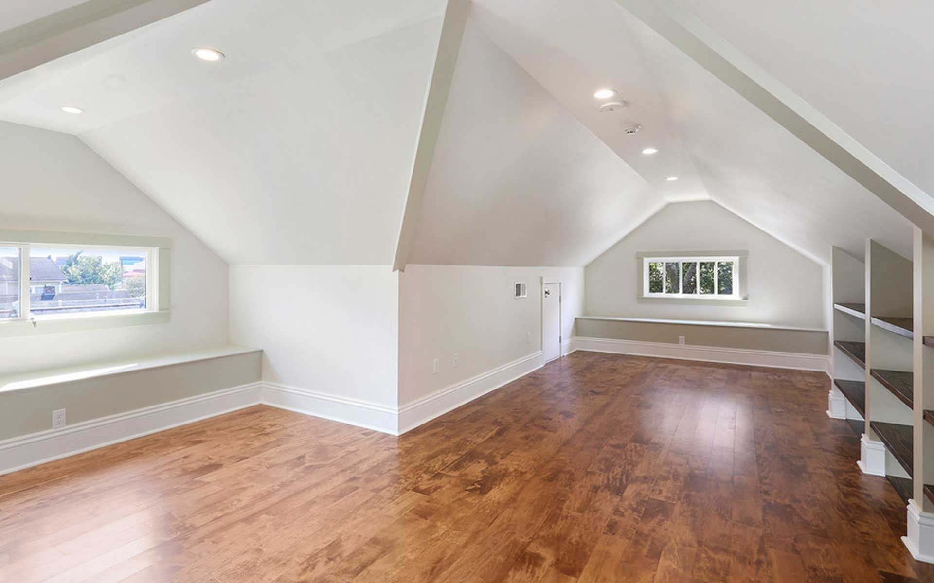 An empty attic with hardwood floors and white walls.