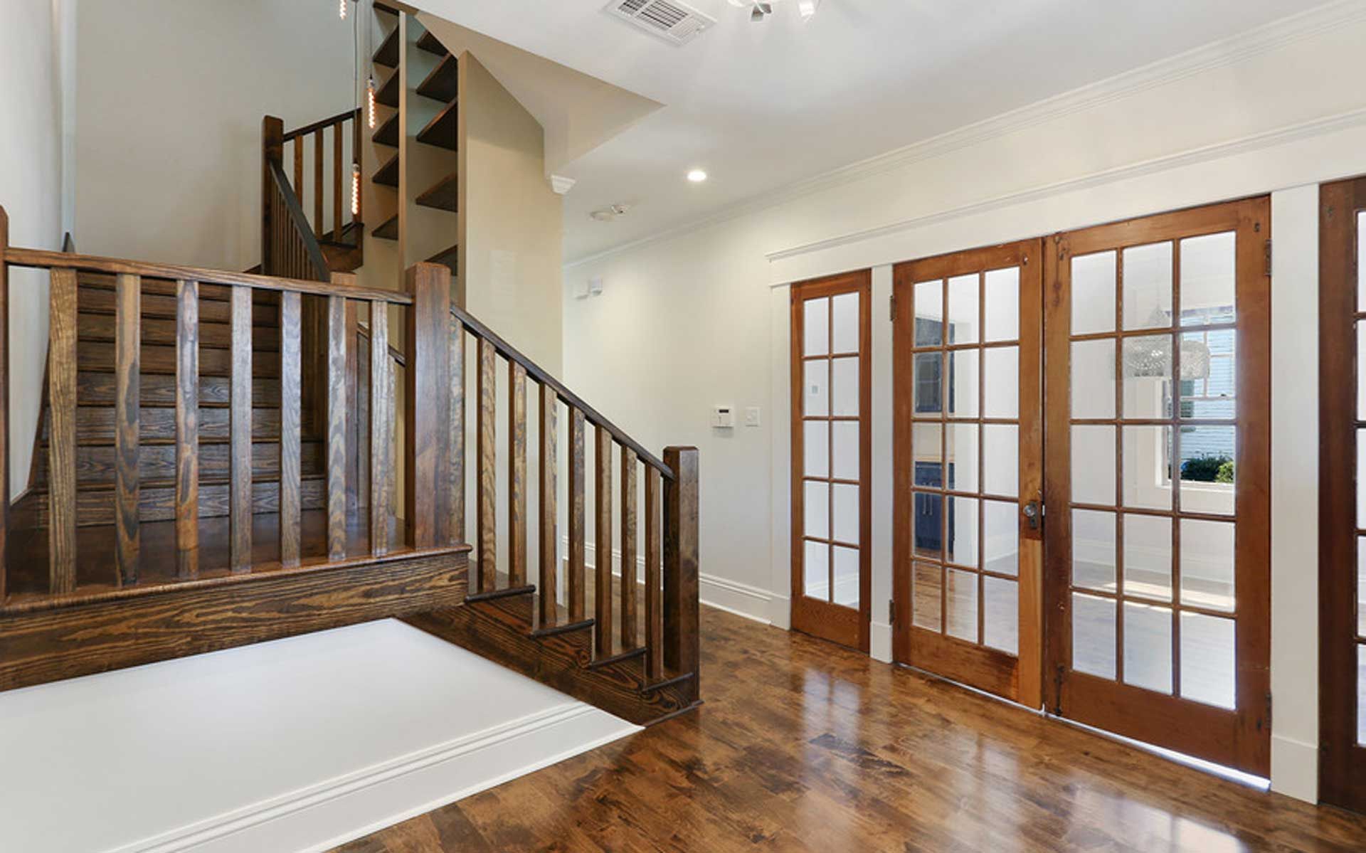 A hallway with hardwood floors , stairs , and french doors.
