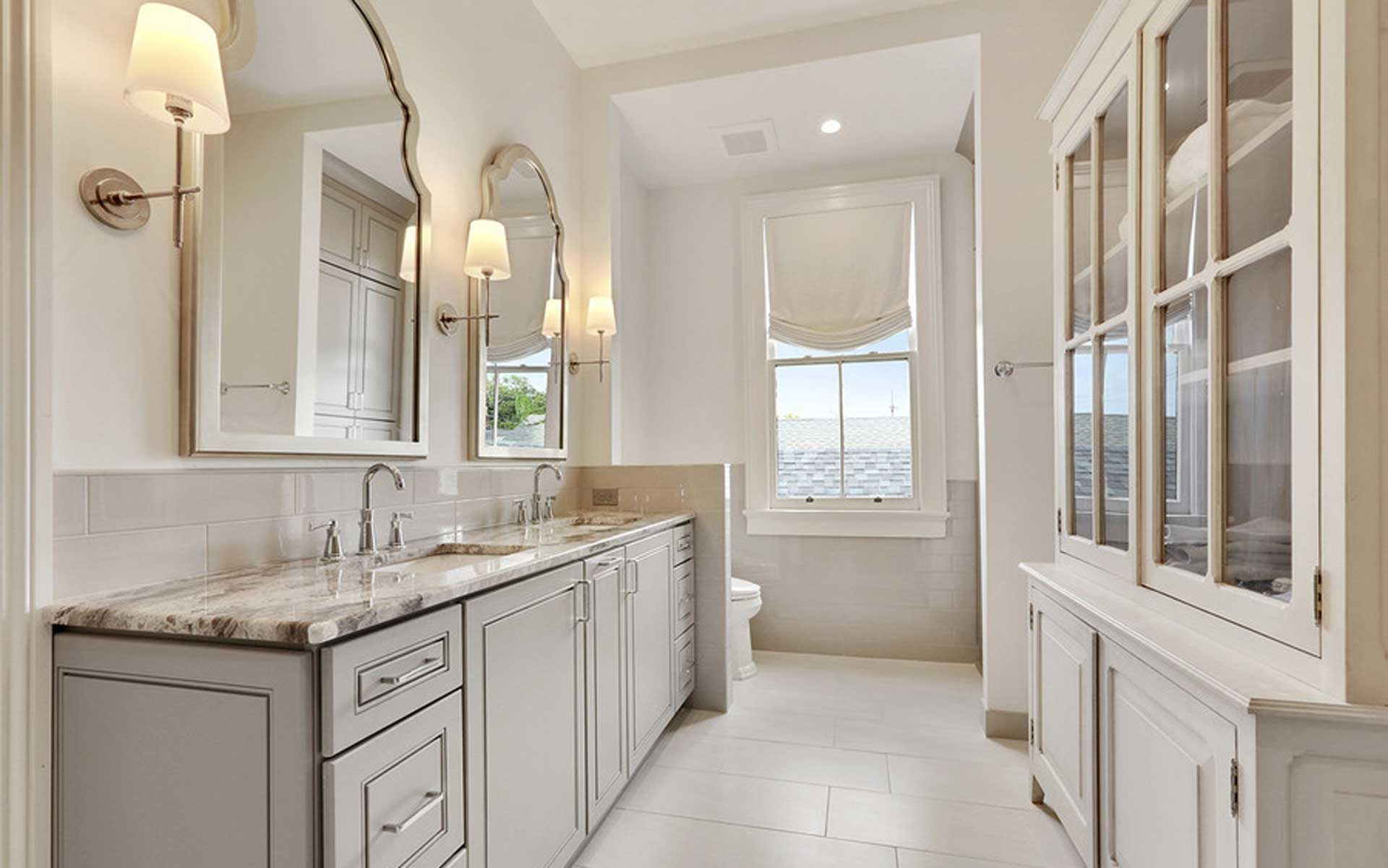 A bathroom with two sinks , two mirrors , a toilet and a window.