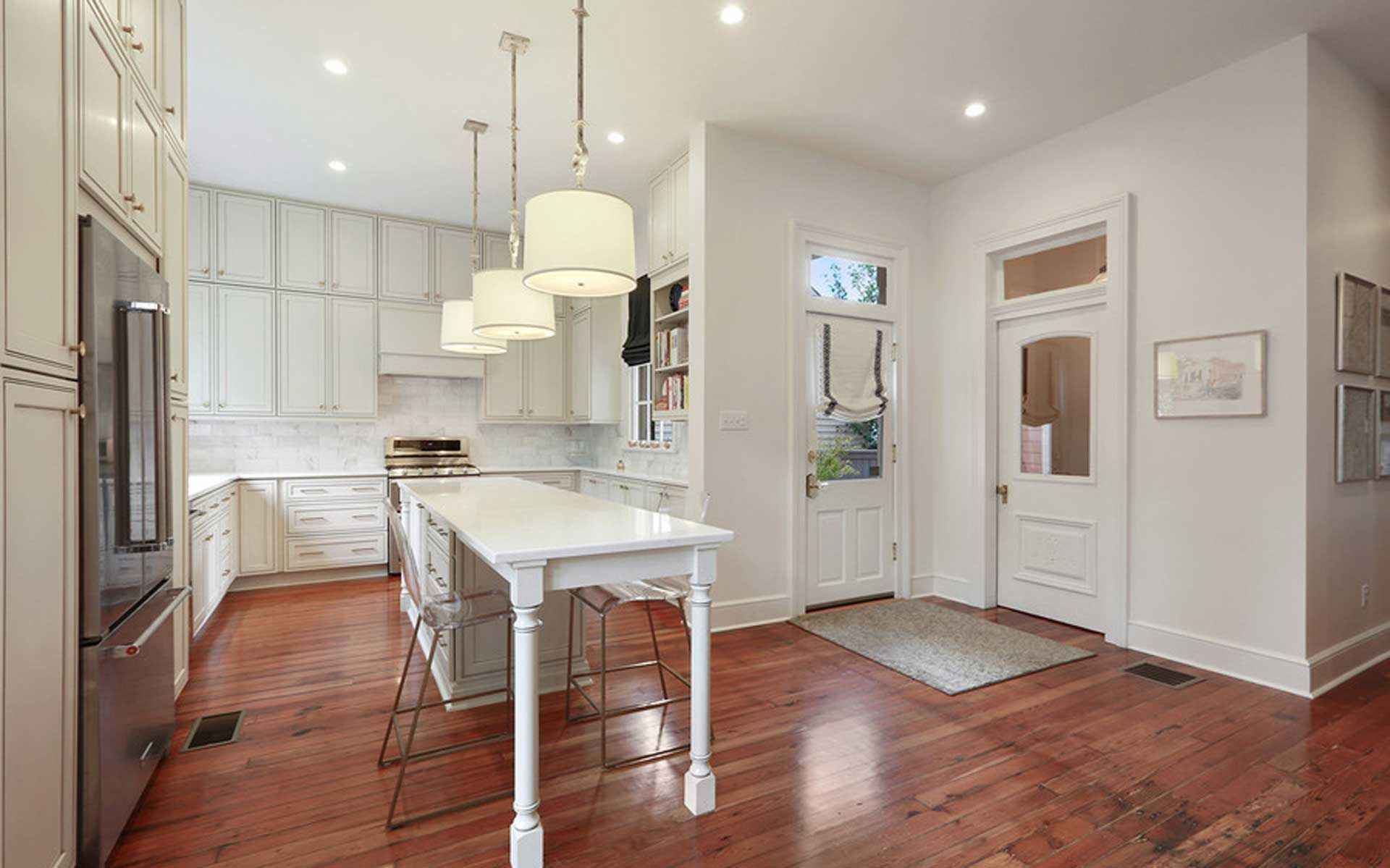 A kitchen with white cabinets , stainless steel appliances , hardwood floors and a long white table.