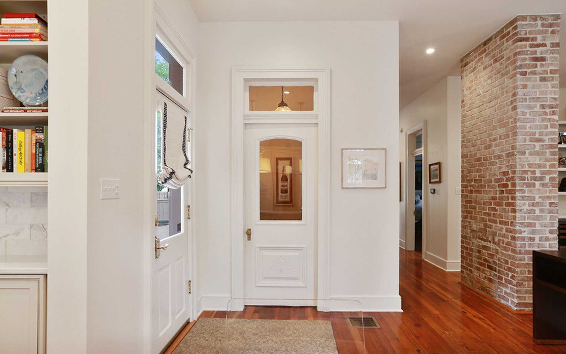 A hallway with a white door and a brick wall.