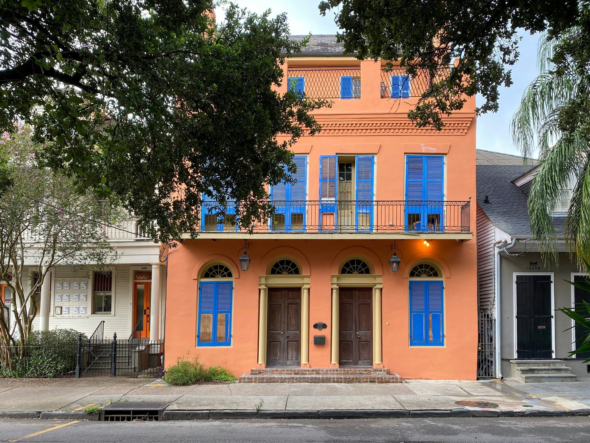 Yellow apartment building with iron balconies; a red car, person walking on sidewalk.