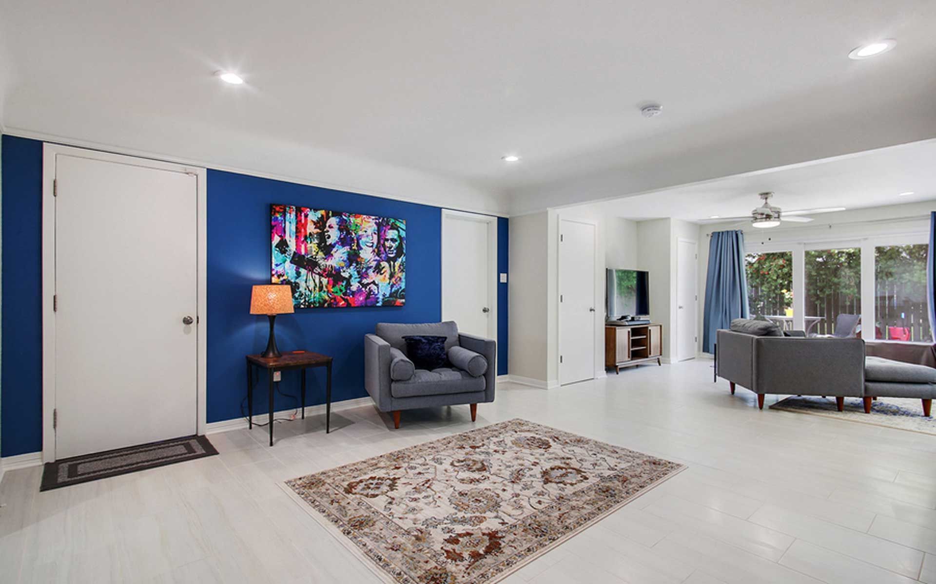 A living room with blue walls , a rug , a couch , a chair and a painting on the wall.