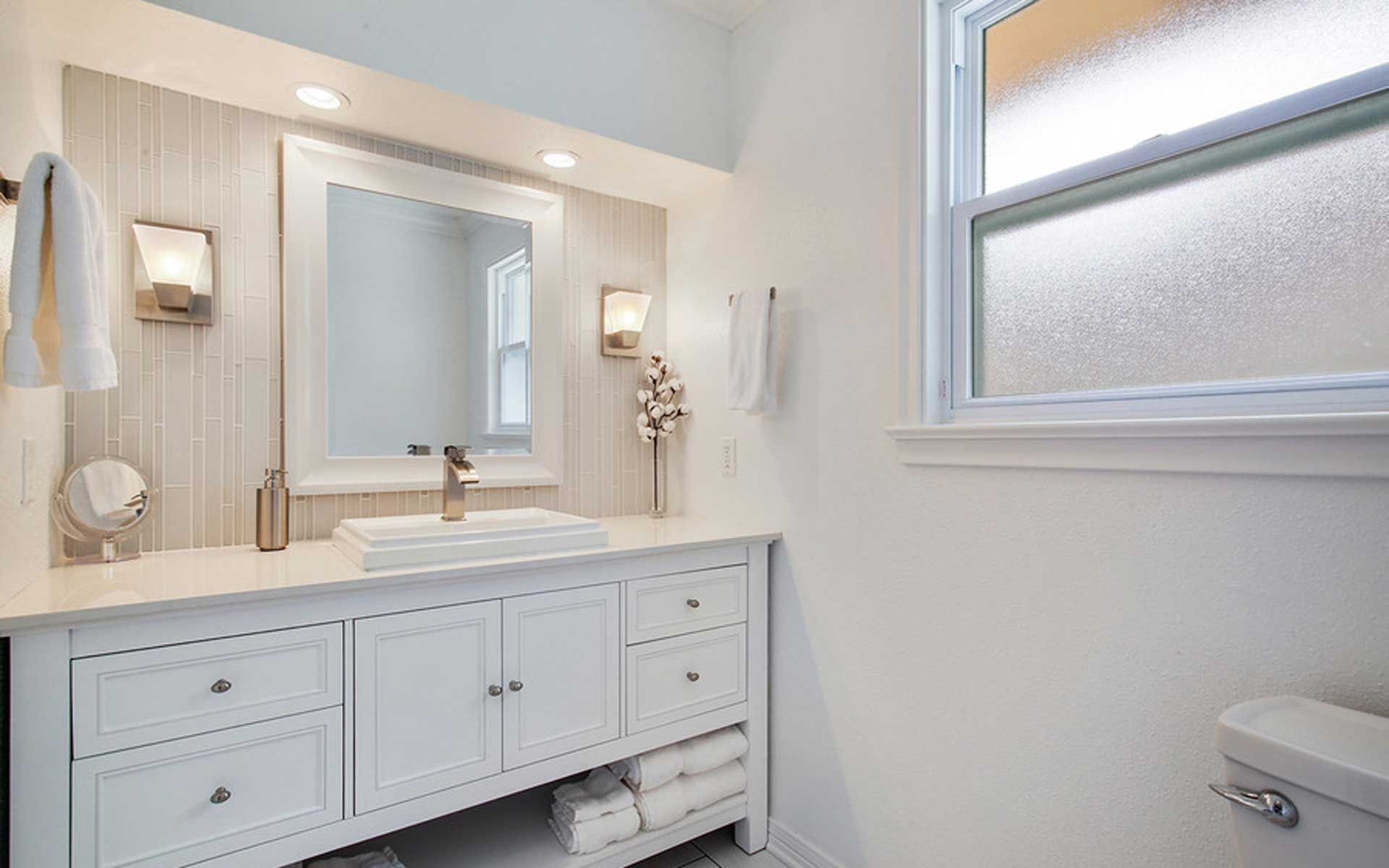 A bathroom with a sink , mirror , toilet and window.