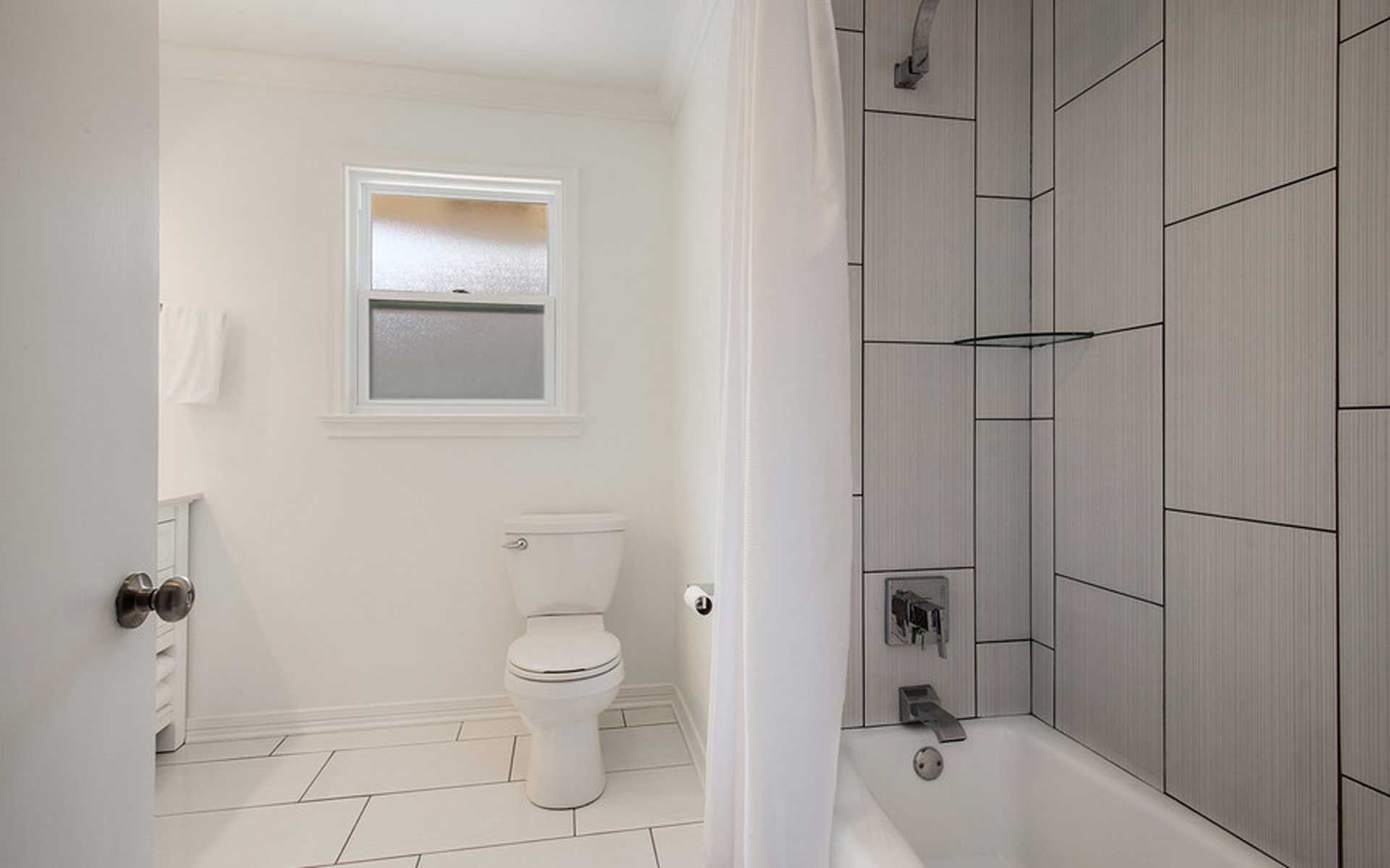 A bathroom with a toilet , tub , shower and window.