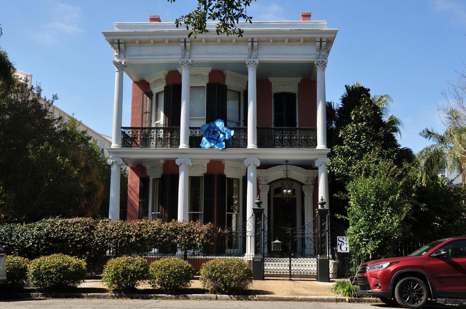 Yellow apartment building with iron balconies; a red car, person walking on sidewalk.