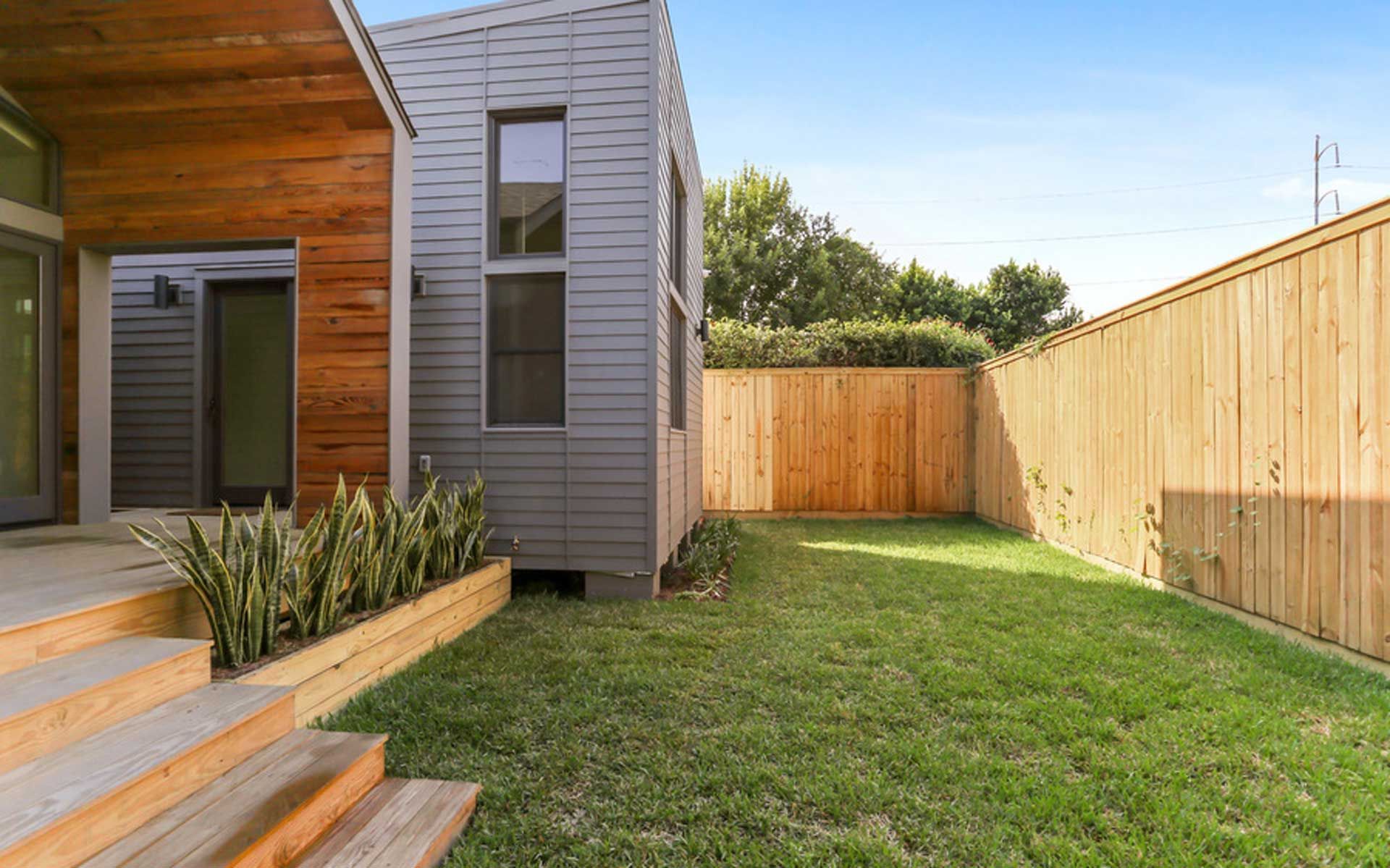 The backyard of a house with a wooden fence and a lush green lawn.