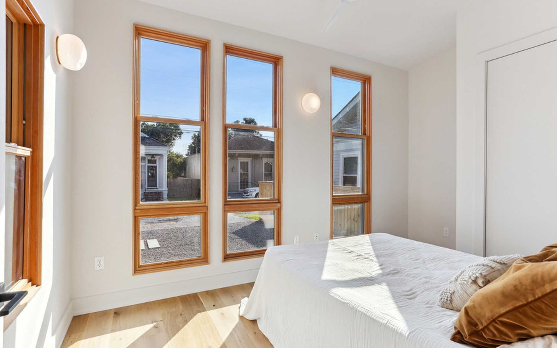 A bedroom with a bed and three windows with a view of a house.