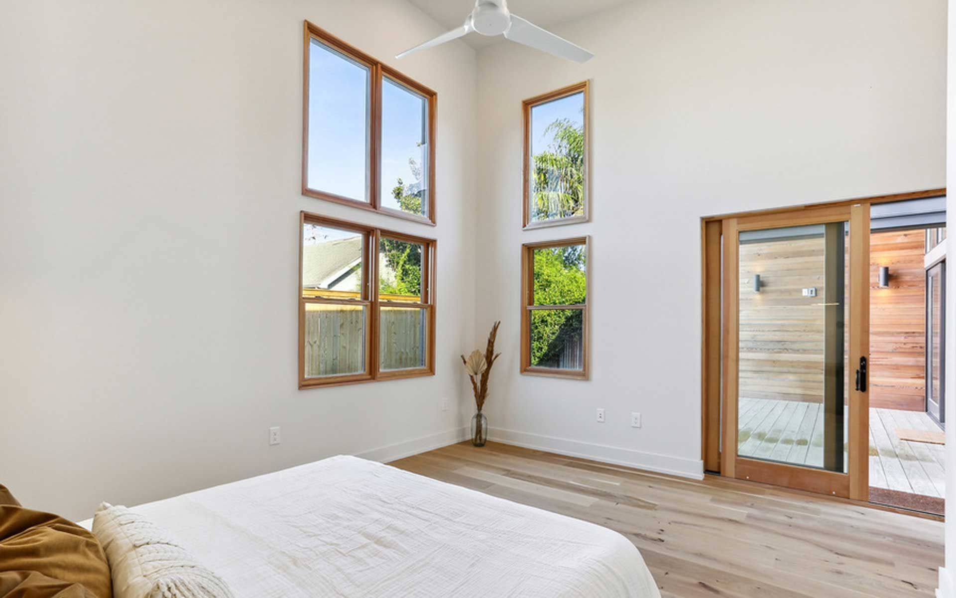 A bedroom with a bed , ceiling fan , and lots of windows.