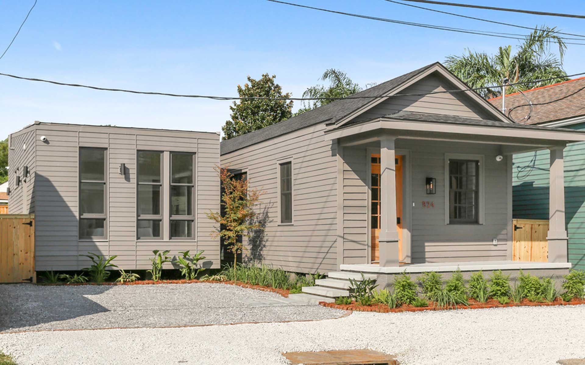 A small house with a porch and a smaller house in the background.