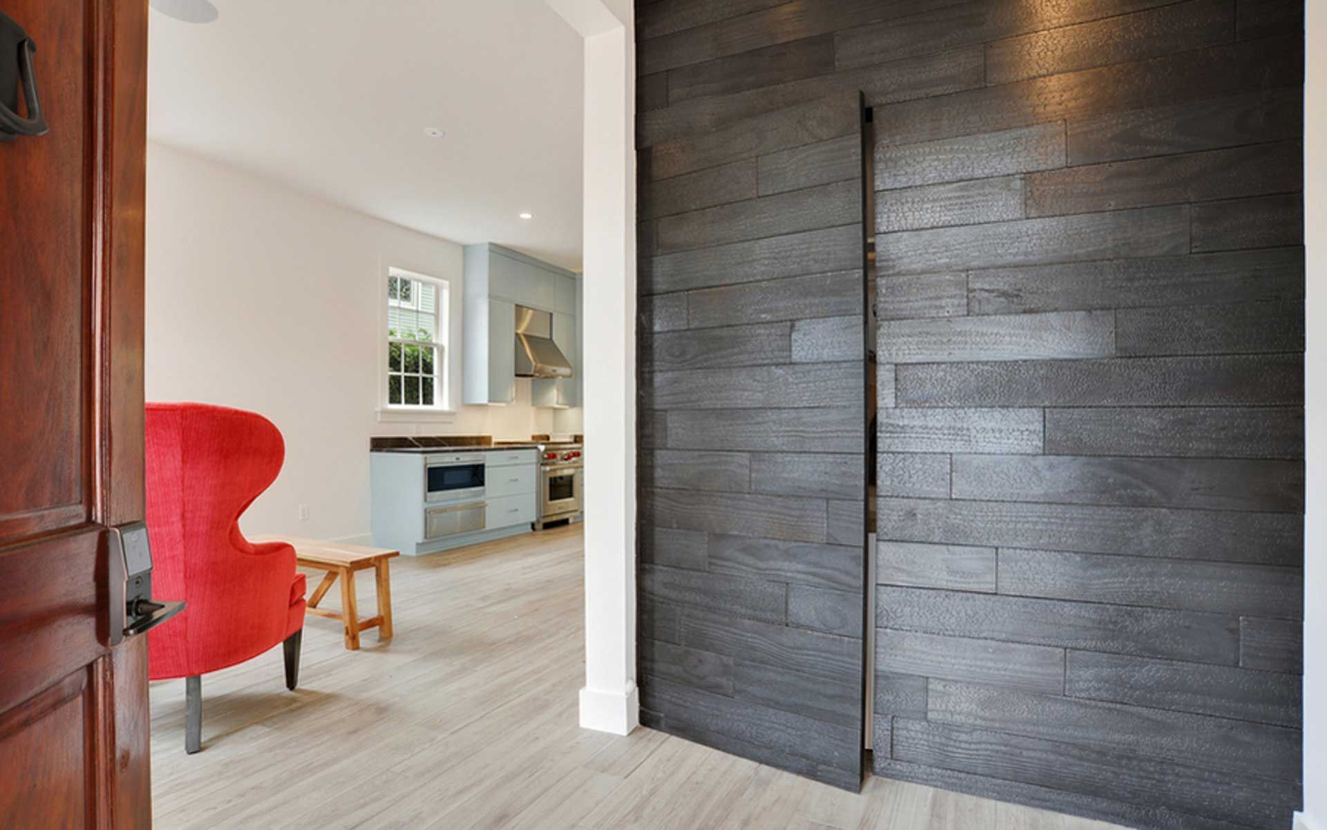 A living room with a red chair and a black door leading to a kitchen.