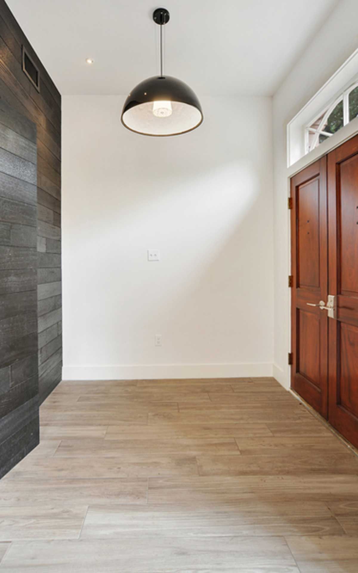 An empty room with wooden floors and a pendant light hanging from the ceiling.