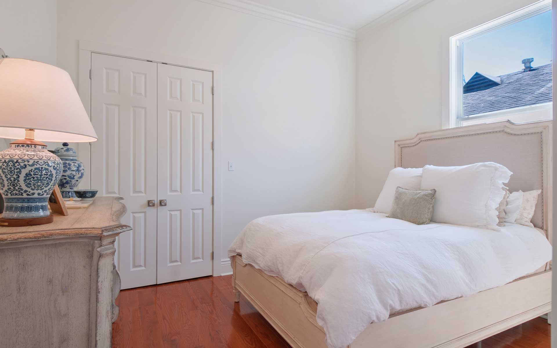 A bedroom with a bed , dresser , lamp and window.