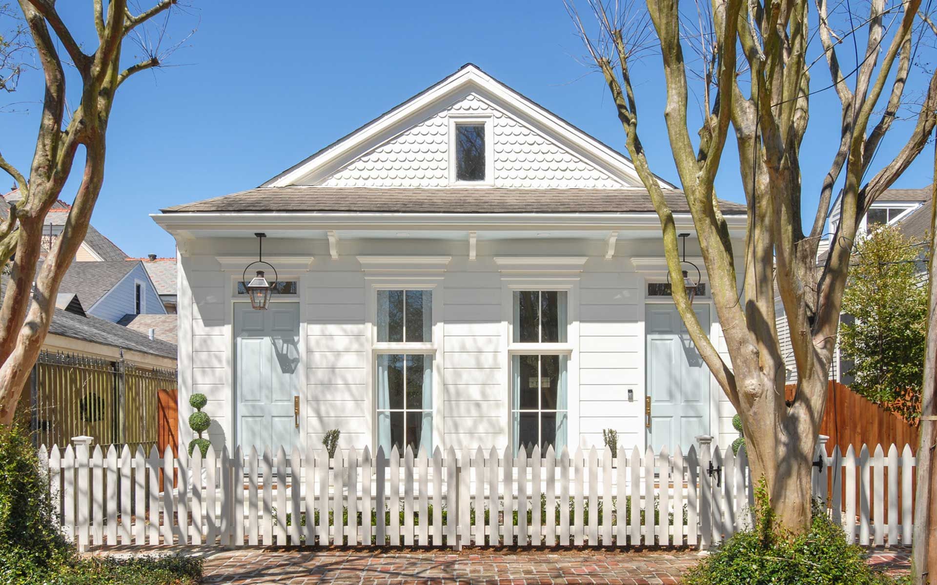 A white house with a white picket fence and trees in front of it.