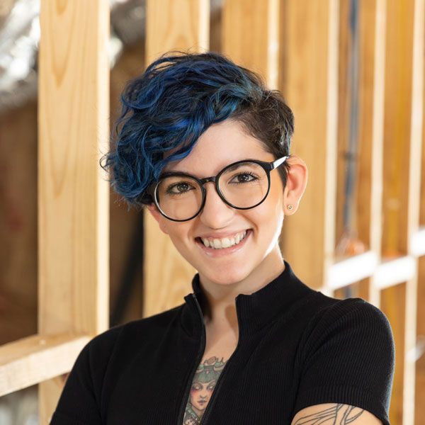 A woman in a pink jacket is standing in front of a red background.
