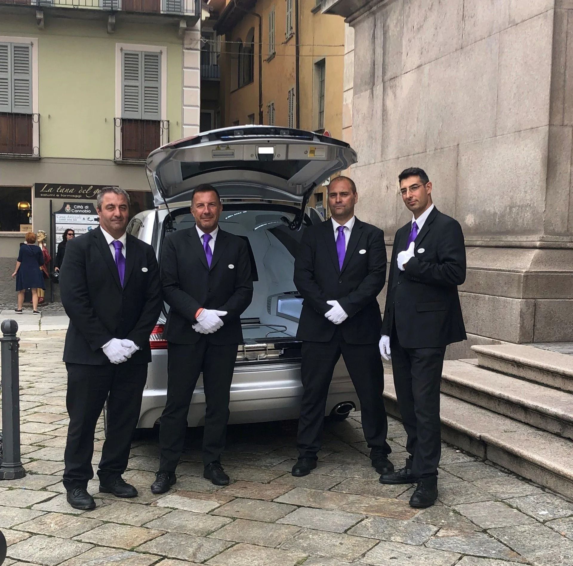 Quattro portatori di bara in abiti formali scuri con cravatte viola e guanti bianchi 