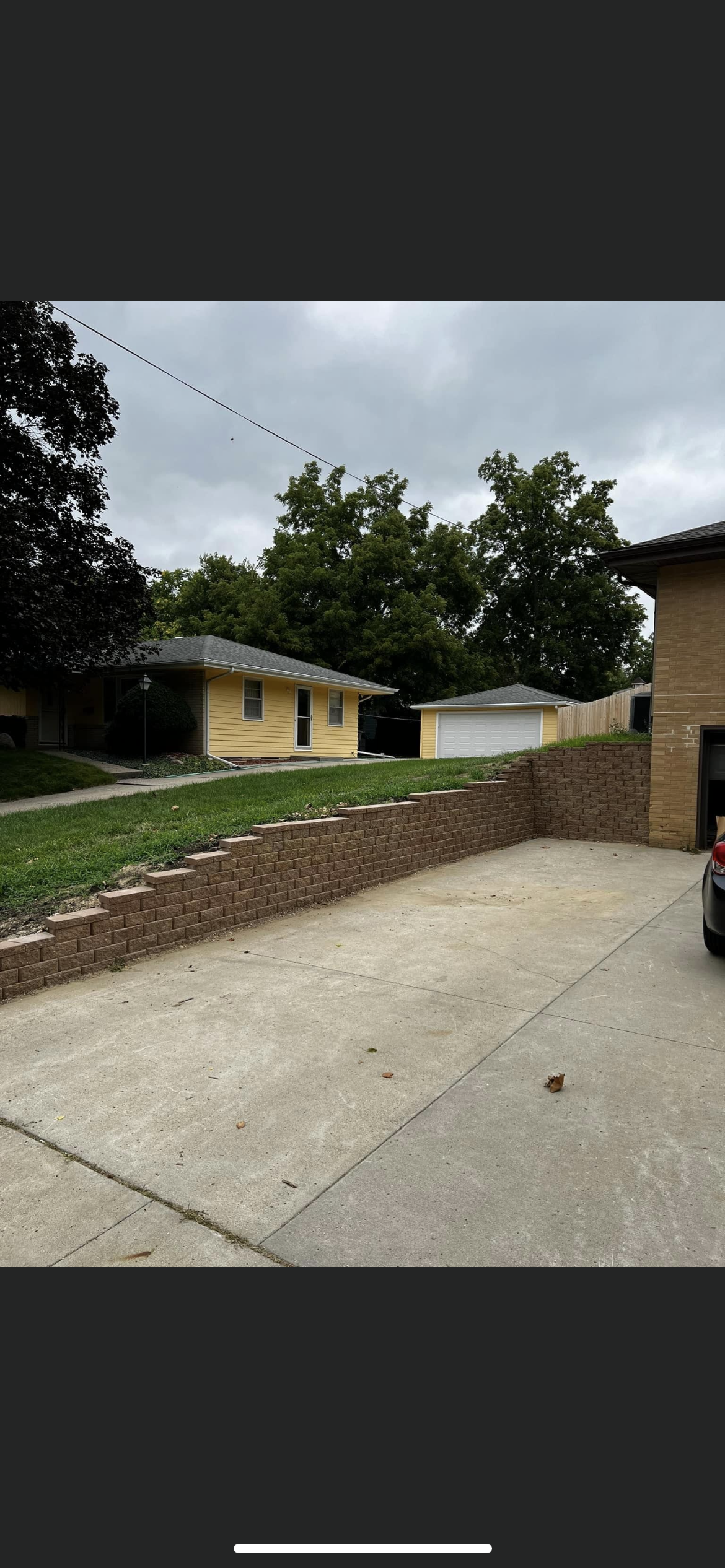 View of a residential property with a yellow house, garage, and driveway on a cloudy day.
