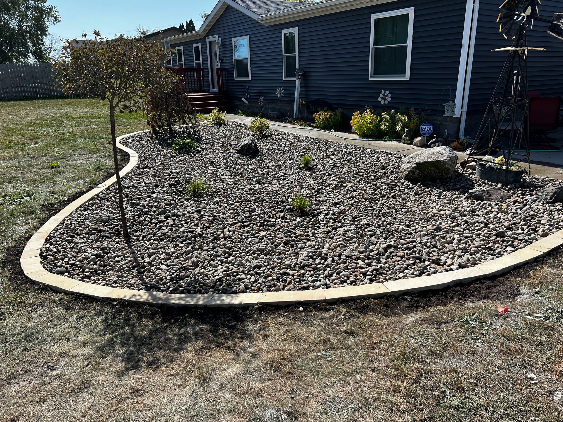 A landscaped yard with gravel, a concrete border, and a house with blue siding.