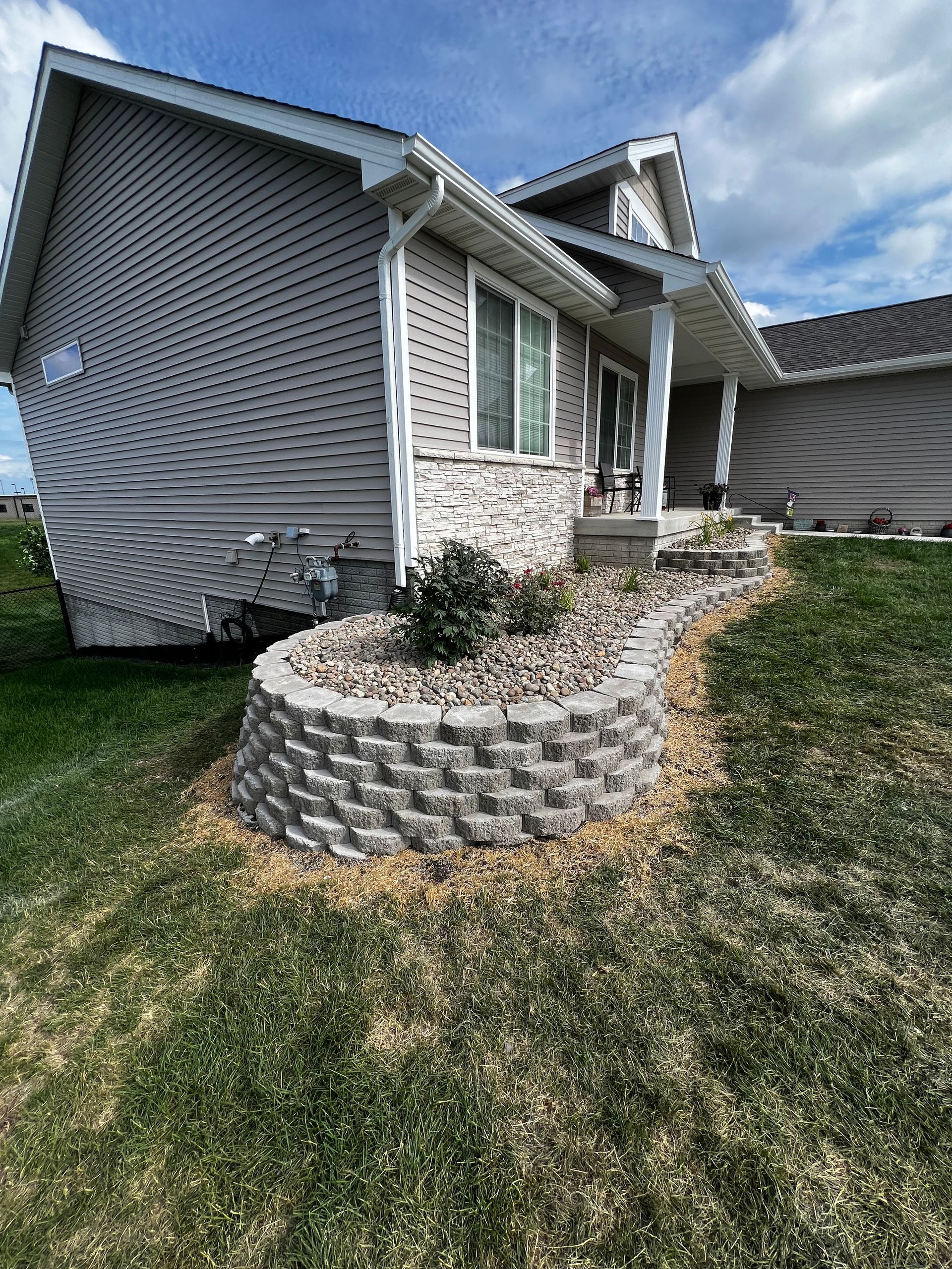 Grey house with stone retaining wall and landscaping.